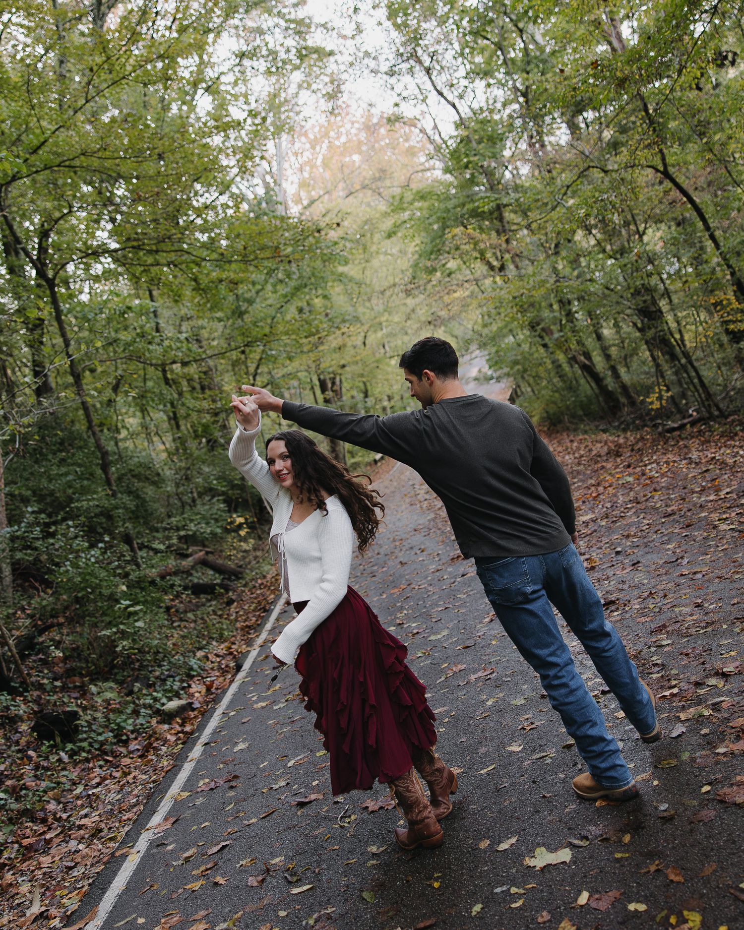 Playful sequence of a couple dancing on a leaf-covered path in autumn.