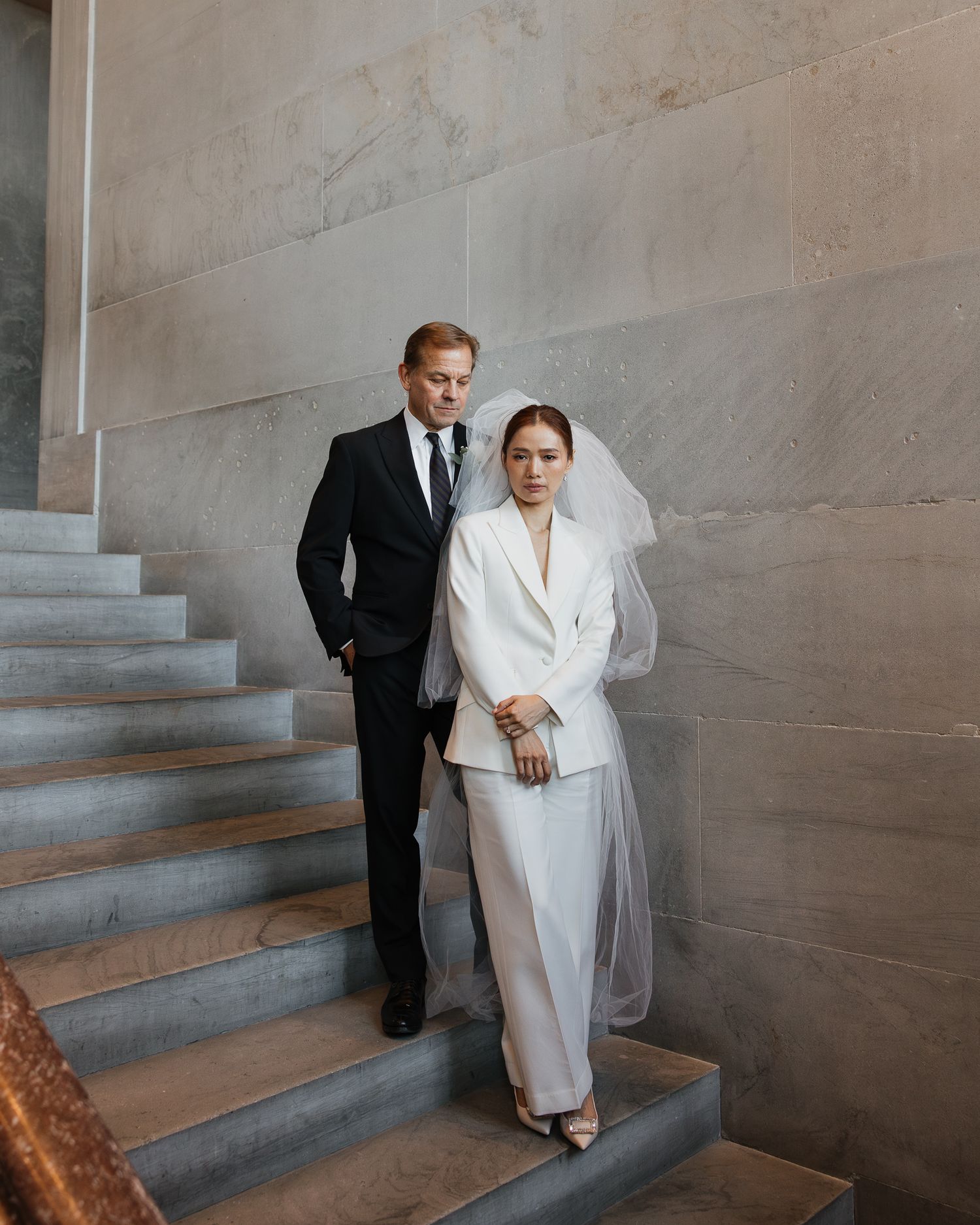Elegant bride in white blazer and veil with groom in black suit posing on marble stairs in the Nashville Tennessee State Capitol.