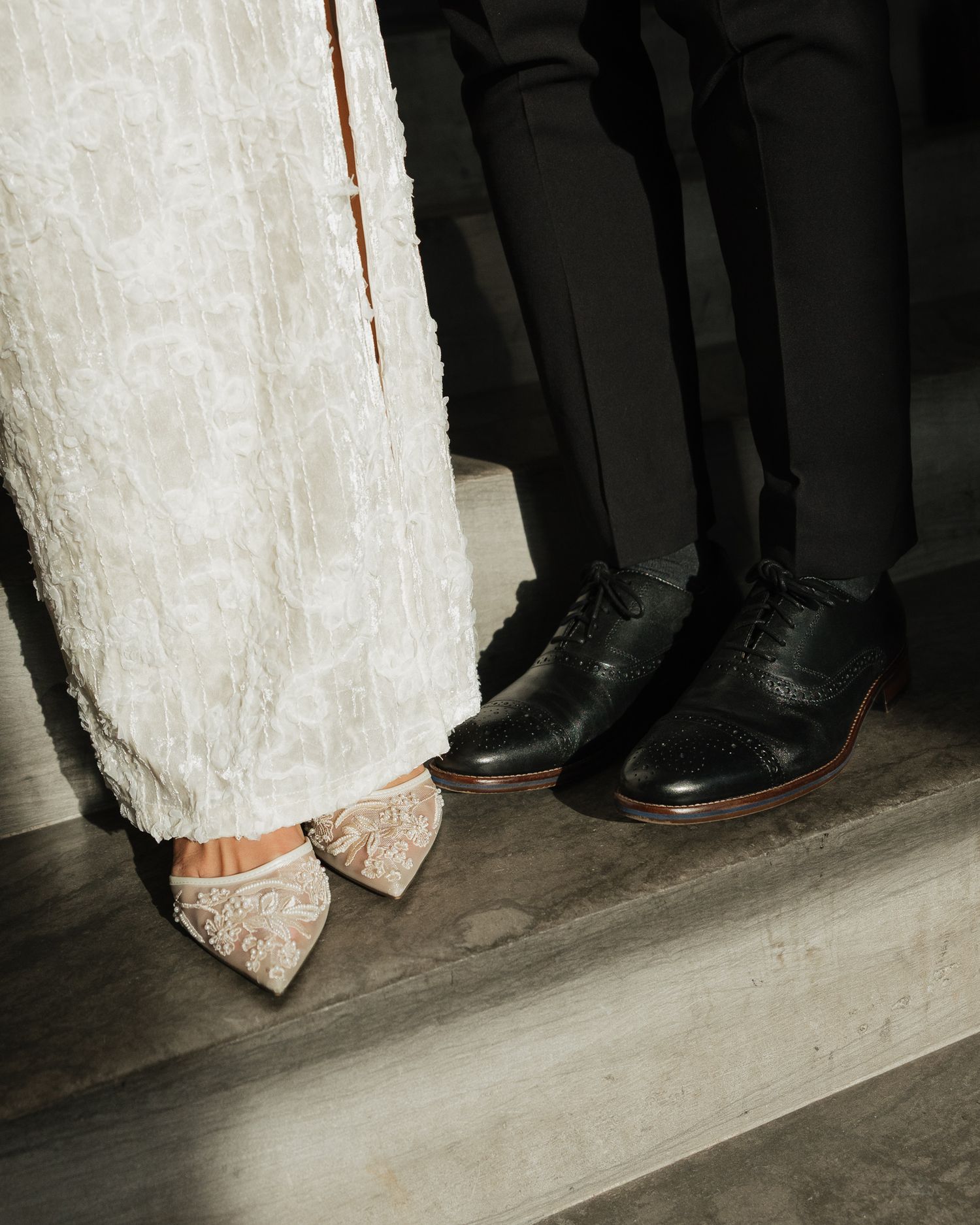 Close-up view of formal shoes and dress hemlines standing in a line on a light colored floor.