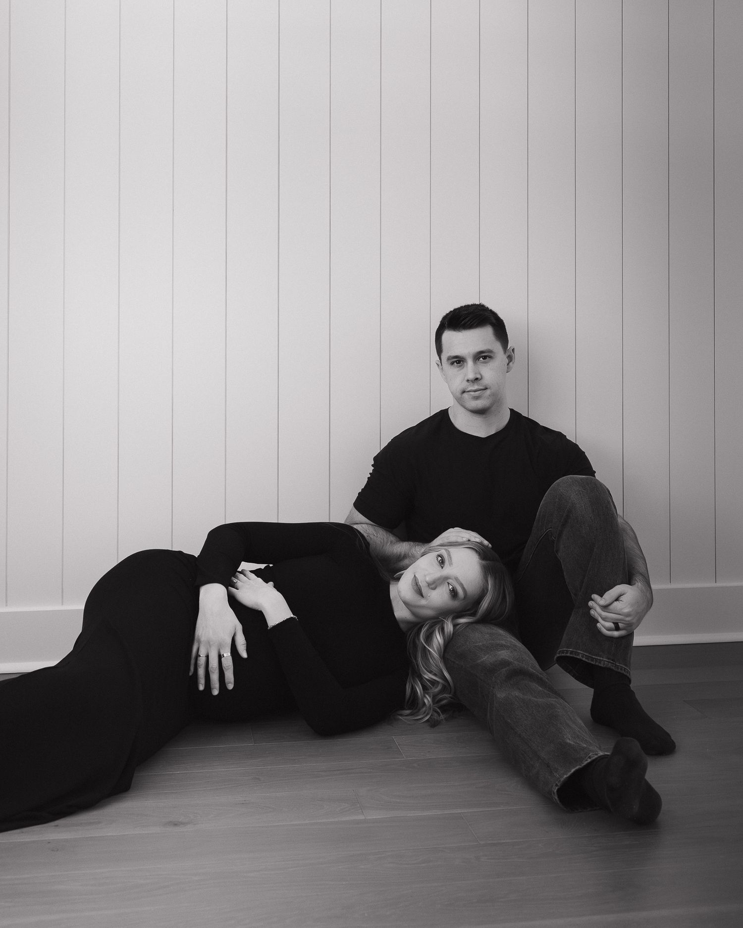 A pregnant woman and her partner in dark clothing reclining on the floor in different poses.