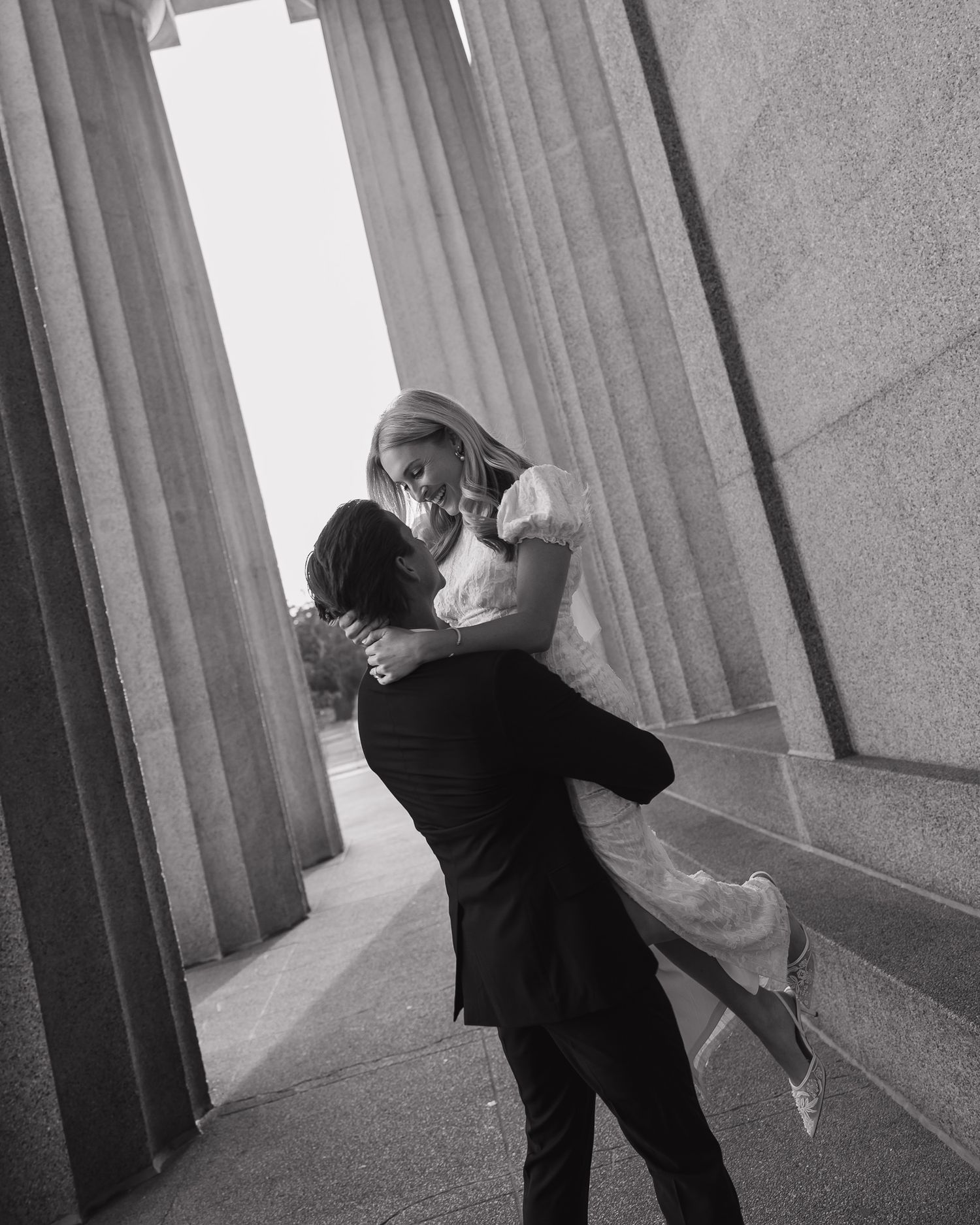 A black and white photo series shows a couple dancing intimately in an elegant columned hallway.