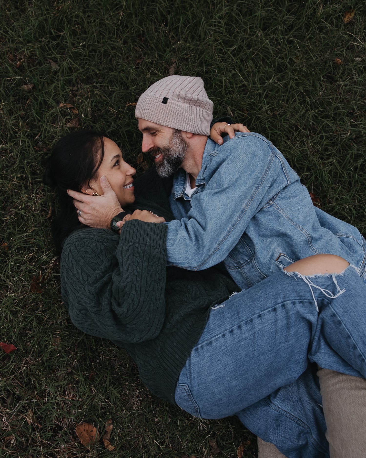 Intimate moments captured between two people in denim and dark sweaters on grass.