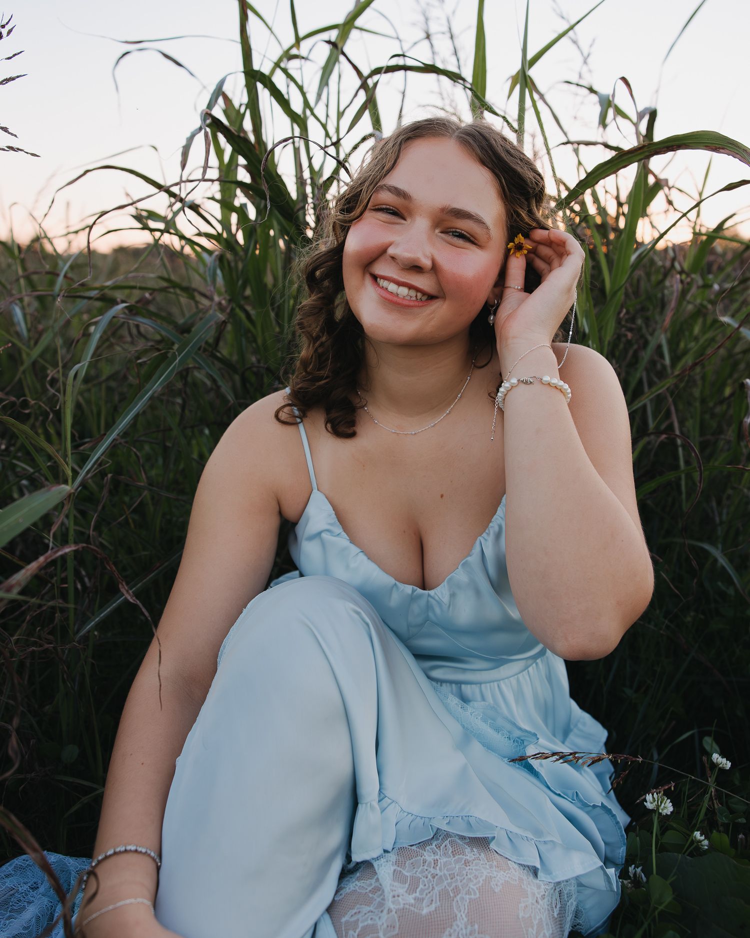 Person in light blue dress smiles while posing in tall grass.