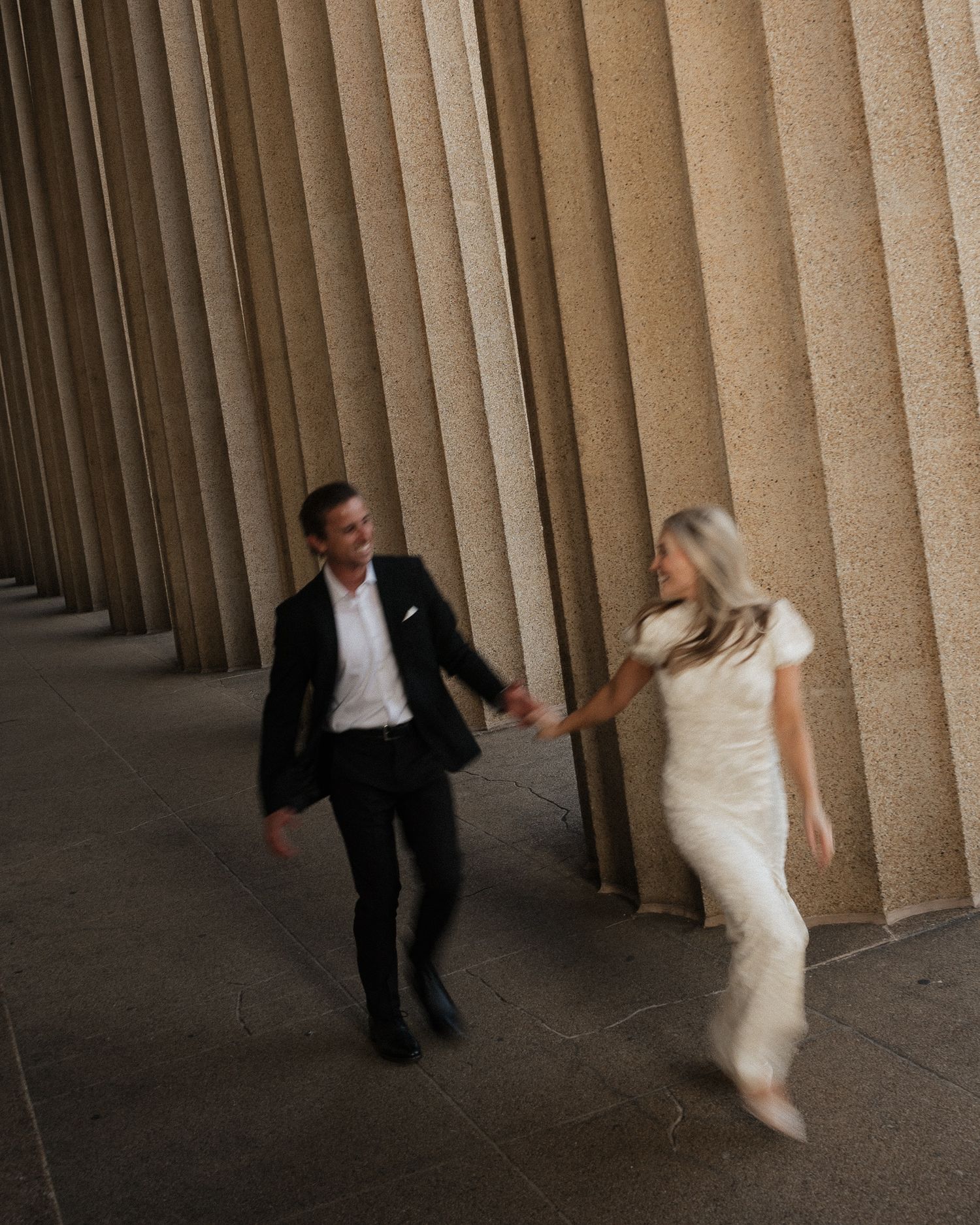 A couple in formal attire performs a playful dance sequence against a backdrop of architectural columns.