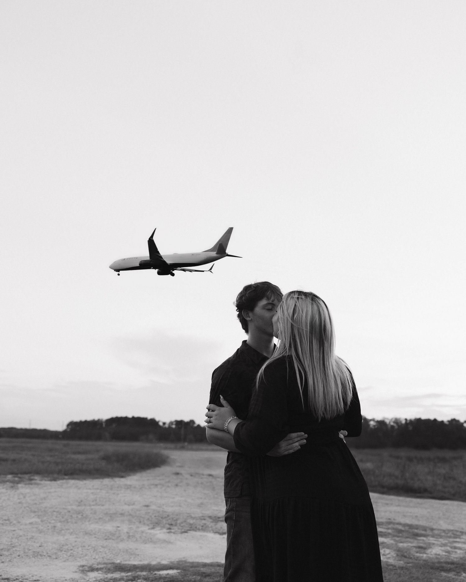 A couple shares an intimate moment while watching a plane fly overhead in a black and white photograph. Tennessee couples photographer