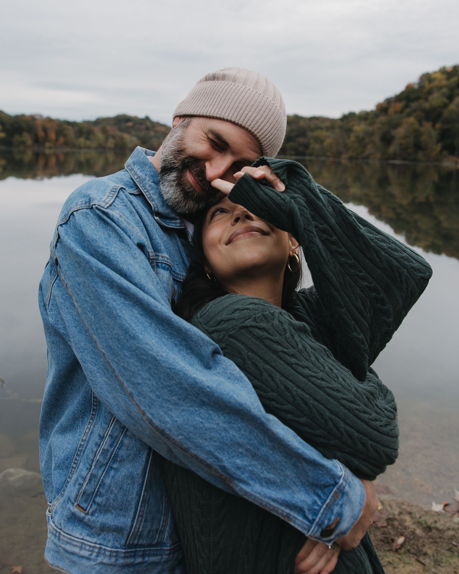 Couple sharing an intimate moment in denim and knitwear against a lakeside backdrop.