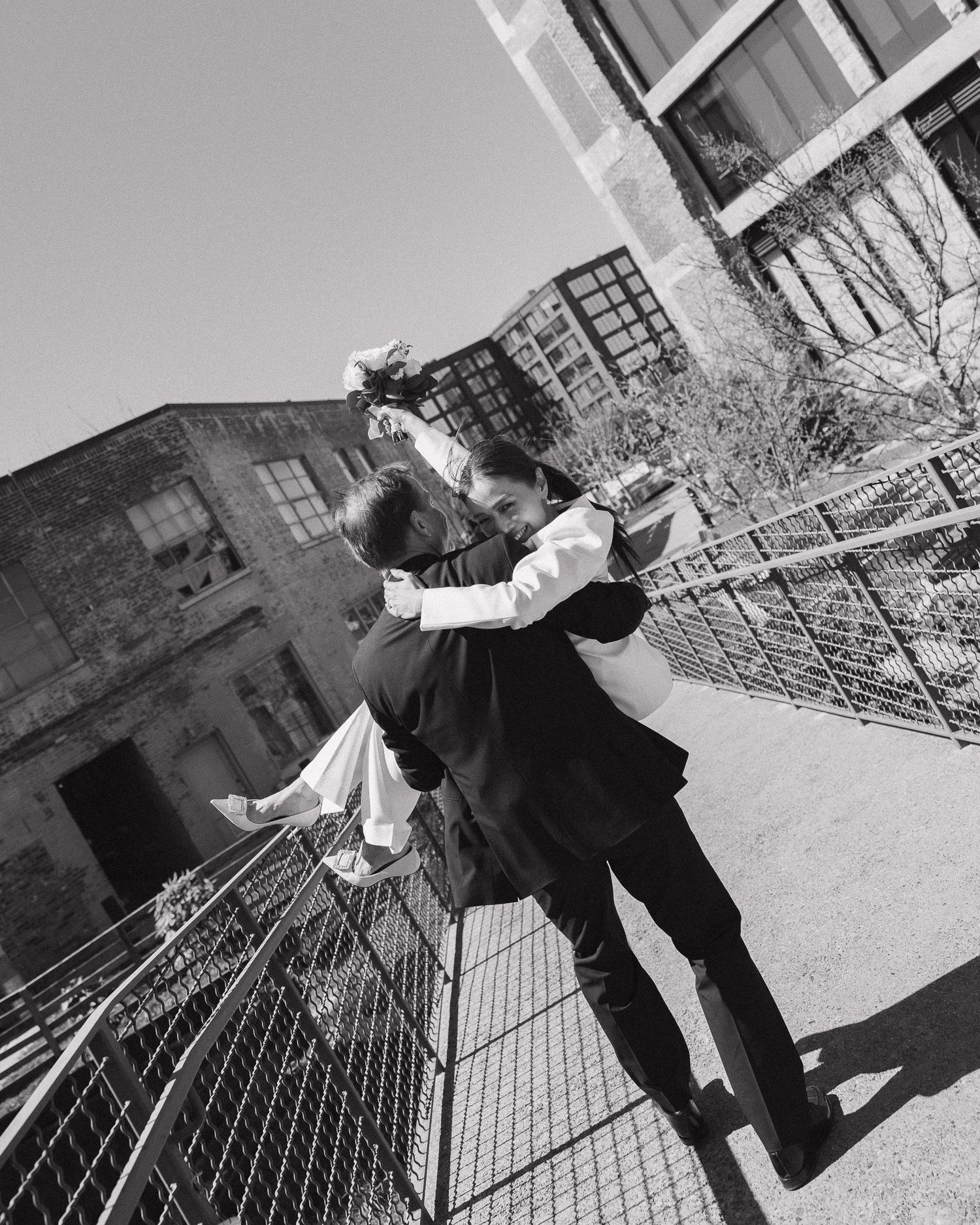 Black and white photo of a couple embracing romantically outdoors on their elopement day near an urban industrial building.