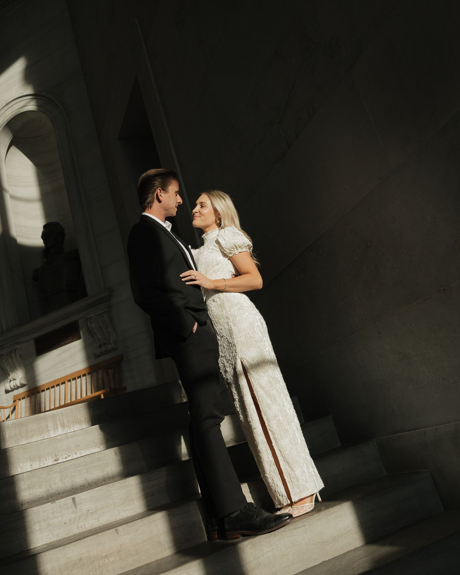 A couple in formal attire shares an intimate moment in dramatic lighting on a staircase.