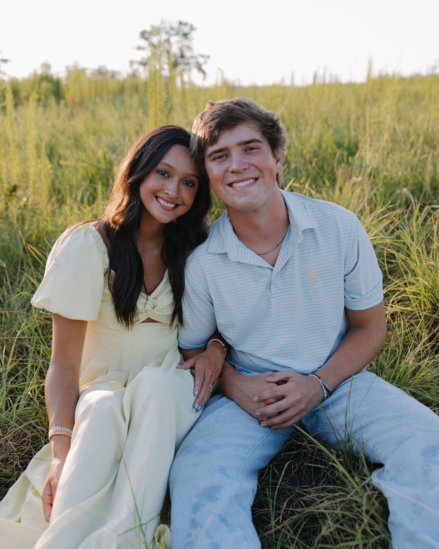 A couple sitting close together in a grassy field during golden hour.
