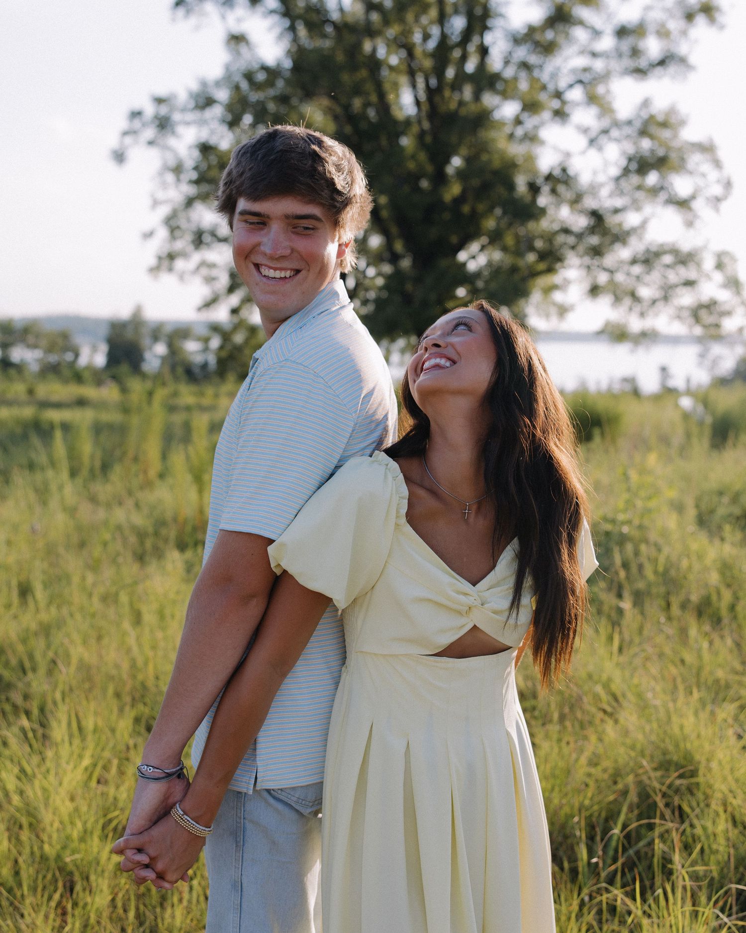 A romantic couple sharing a joyful moment together in a sunny meadow wearing light colored outfits.