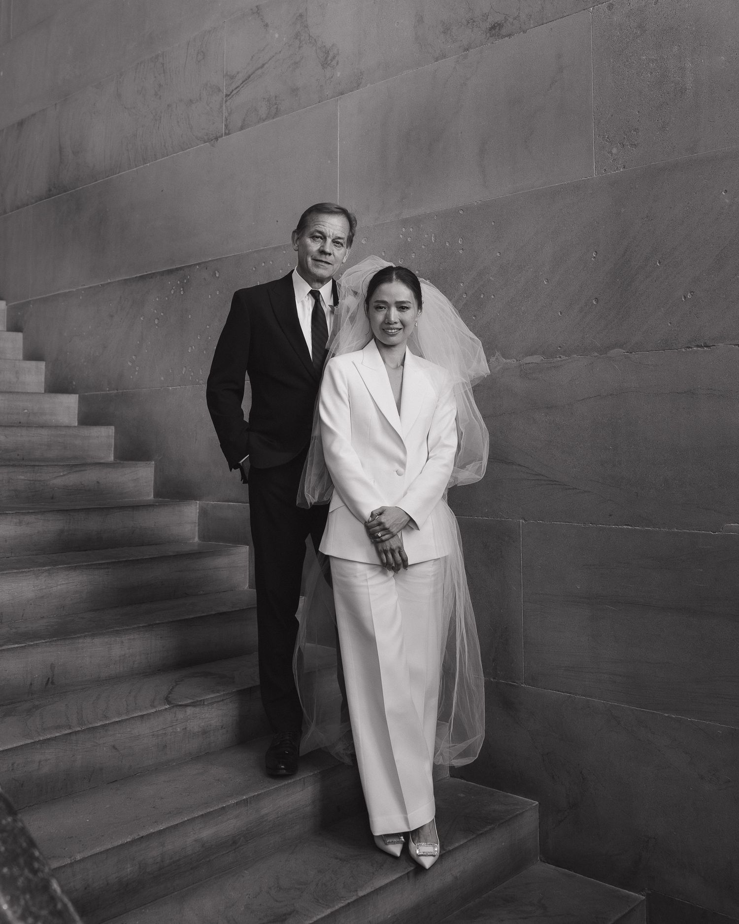 Black and white wedding photo of a couple in elegant attire on stone stairs, bride in white suit with veil in state capitol in Nashville.