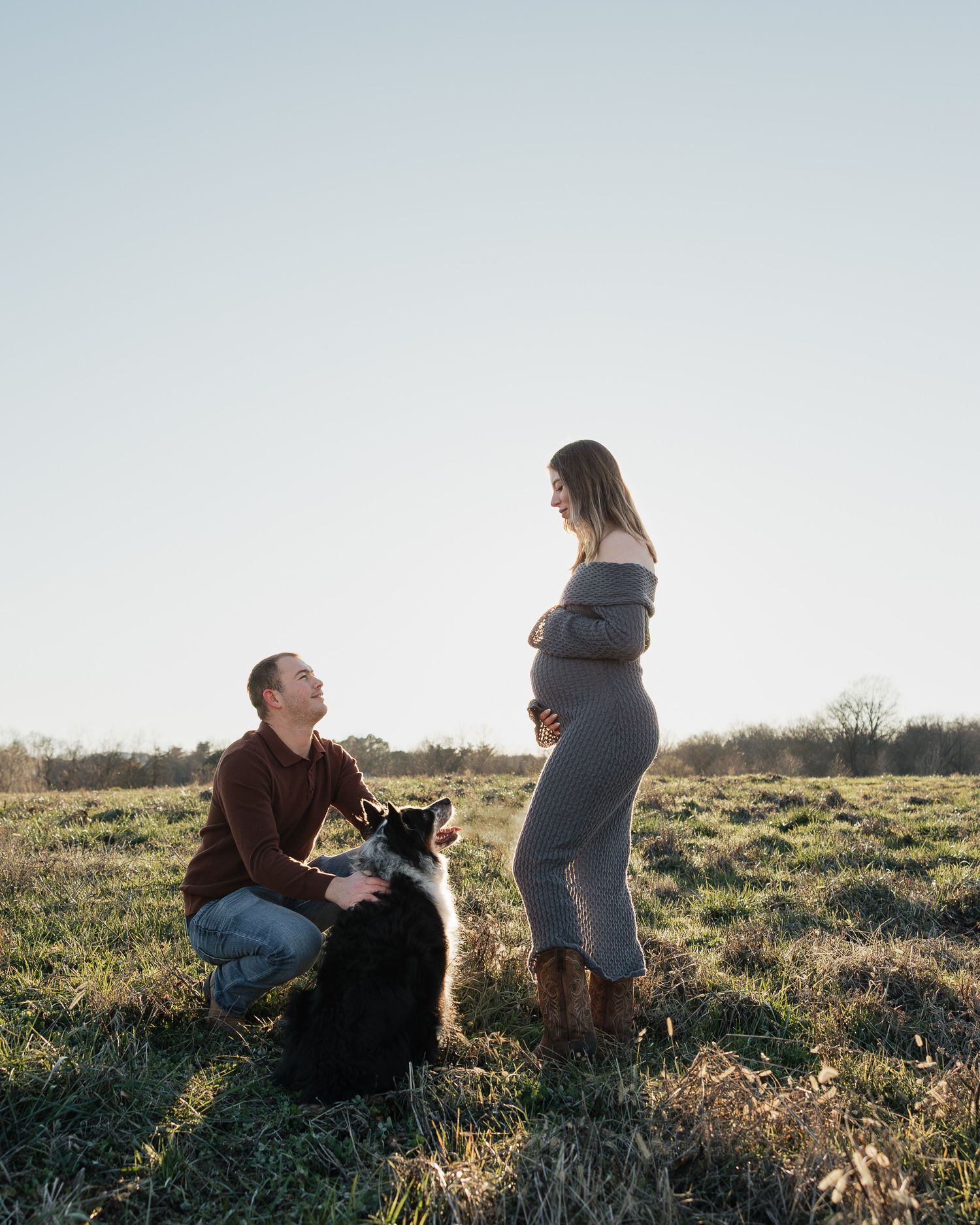 A couple sits together in a grassy field during golden hour as sunlight illuminates the scenic landscape.