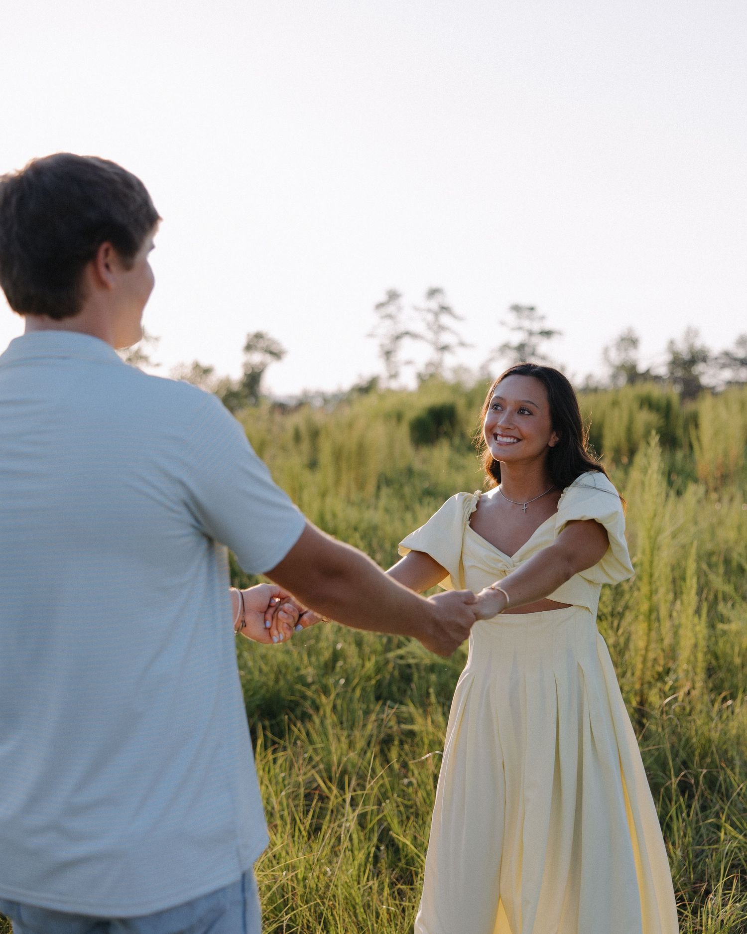 A couple dancing and laughing together in a grassy field during sunset.