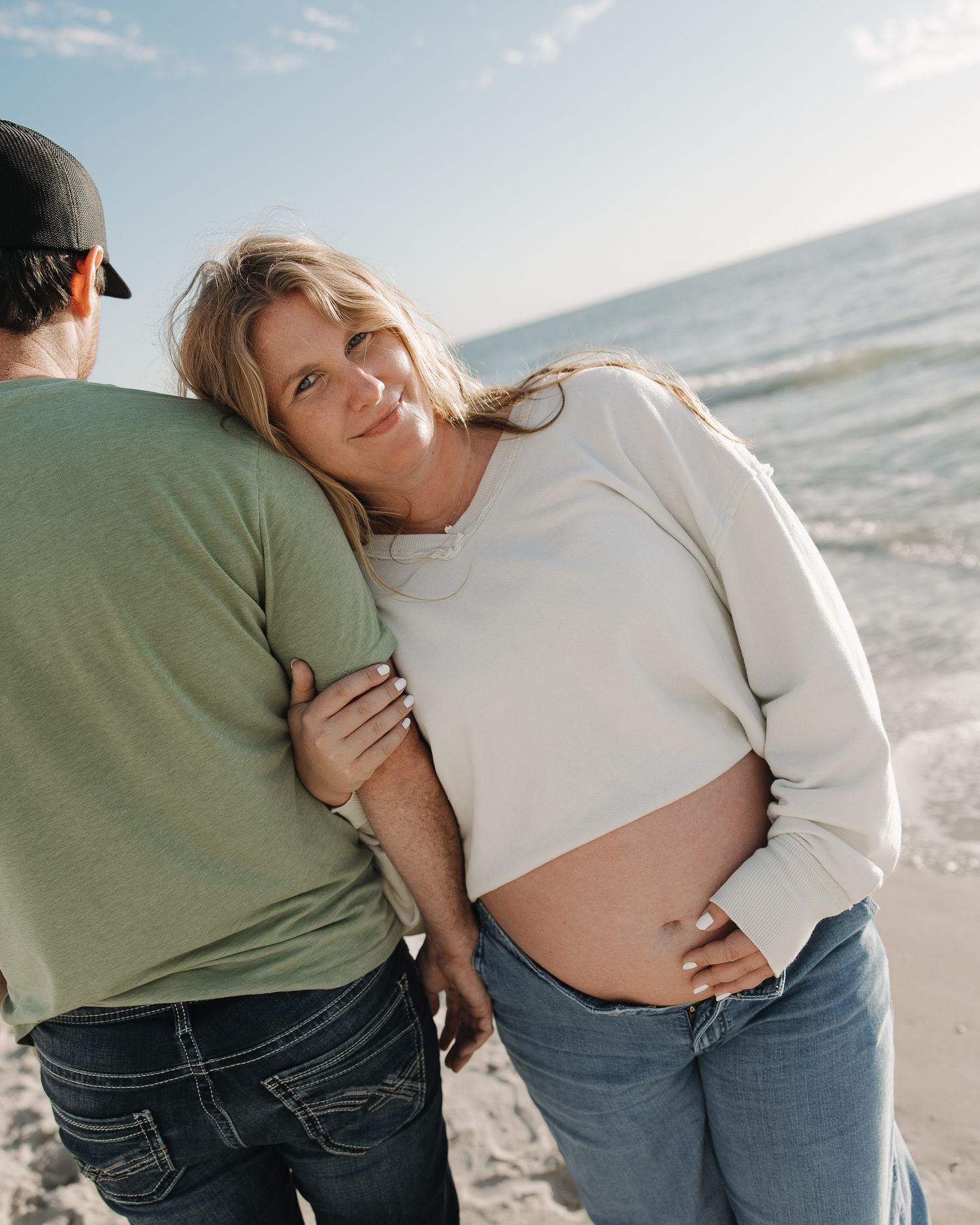 Couple embracing on a sunny beach in casual attire showing affection and closeness.