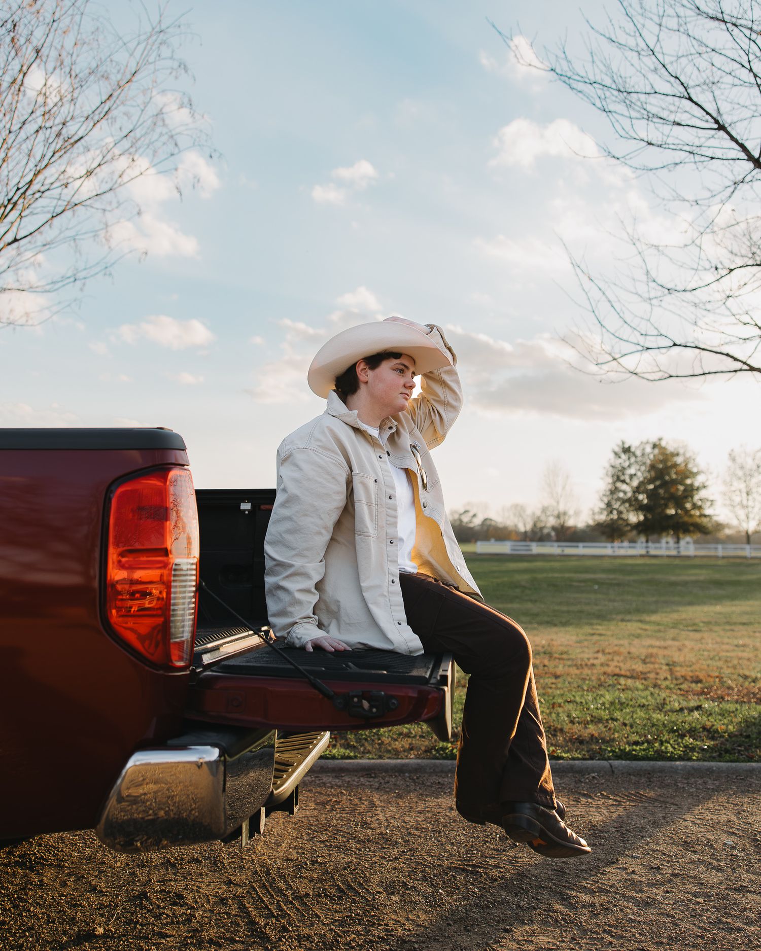Senior boy sit on the back of a pickup truck in a grassy field at sunset photography