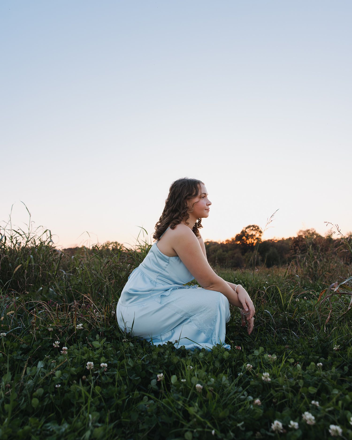 Person in blue dress sits among wildflowers during a sunset photoshoot.