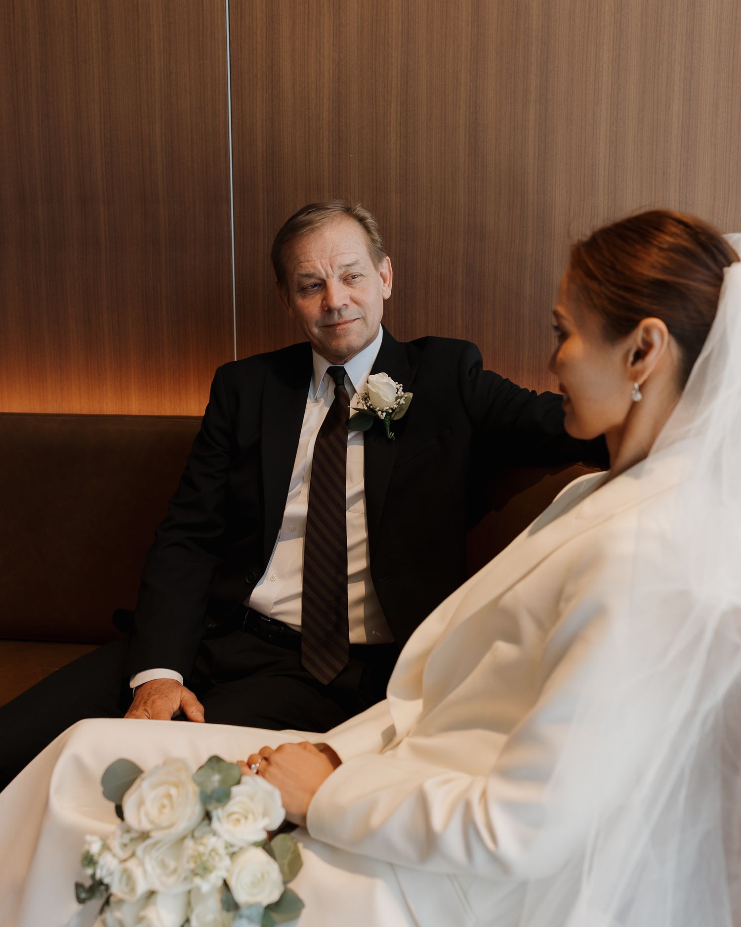 Bride and groom share a tender moment, holding hands before the wedding ceremony, with white floral bouquet.