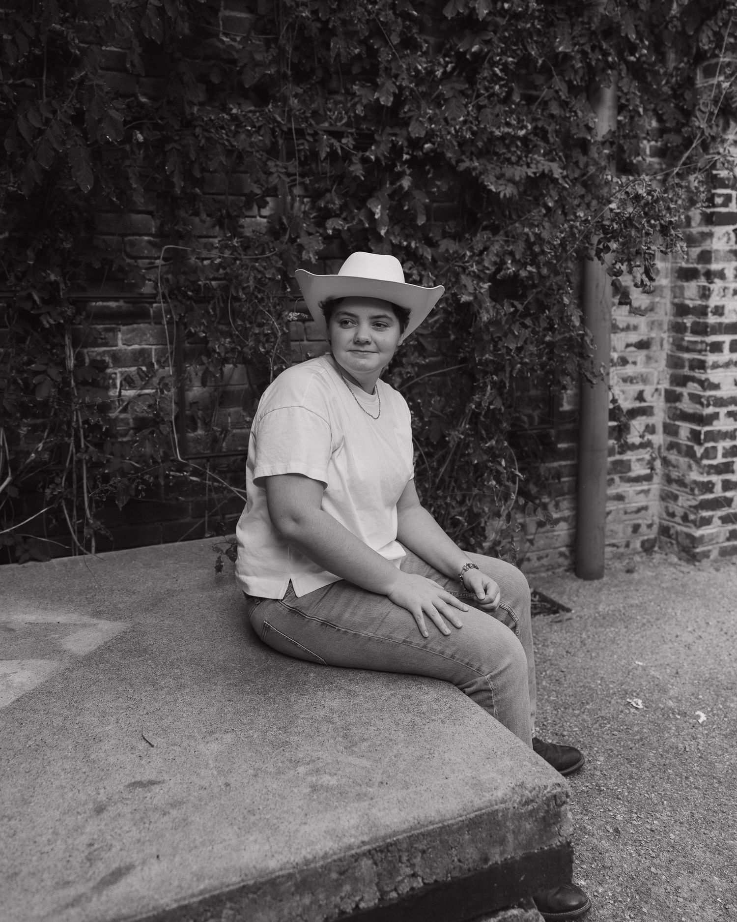 Black and white photo of someone sitting on a stone wall in casual attire.