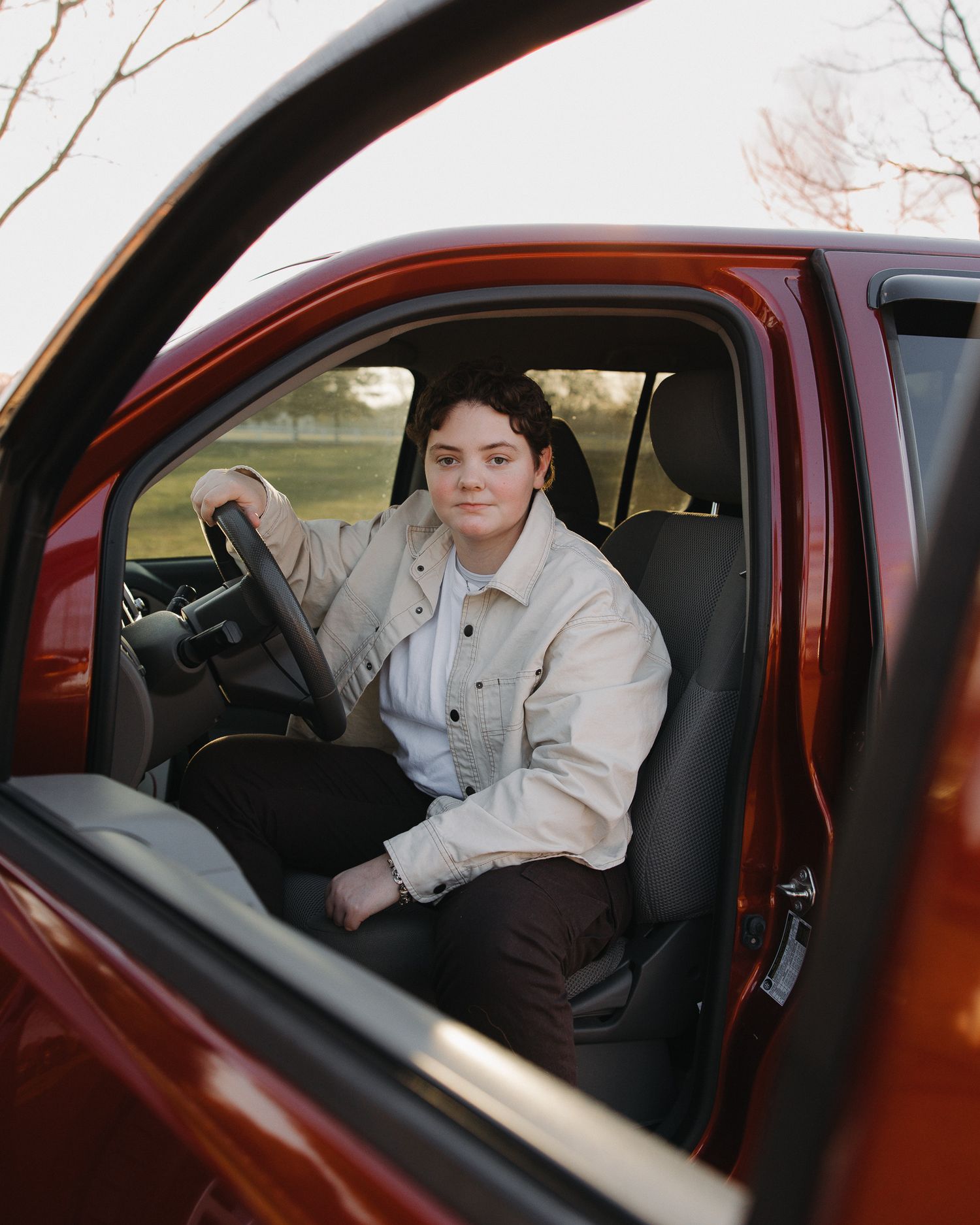 Person in beige jacket poses inside a maroon colored car.