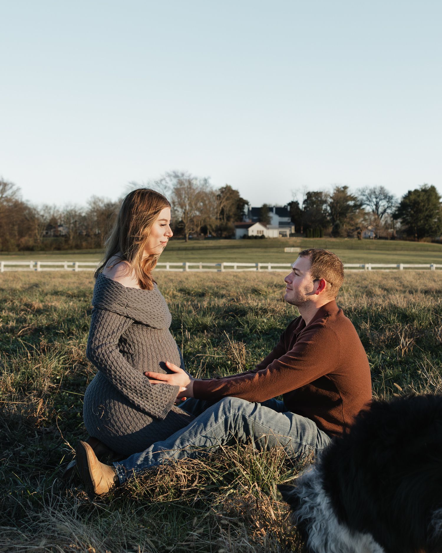 Couple sitting in a grassy field during sunset with their dog nearby.