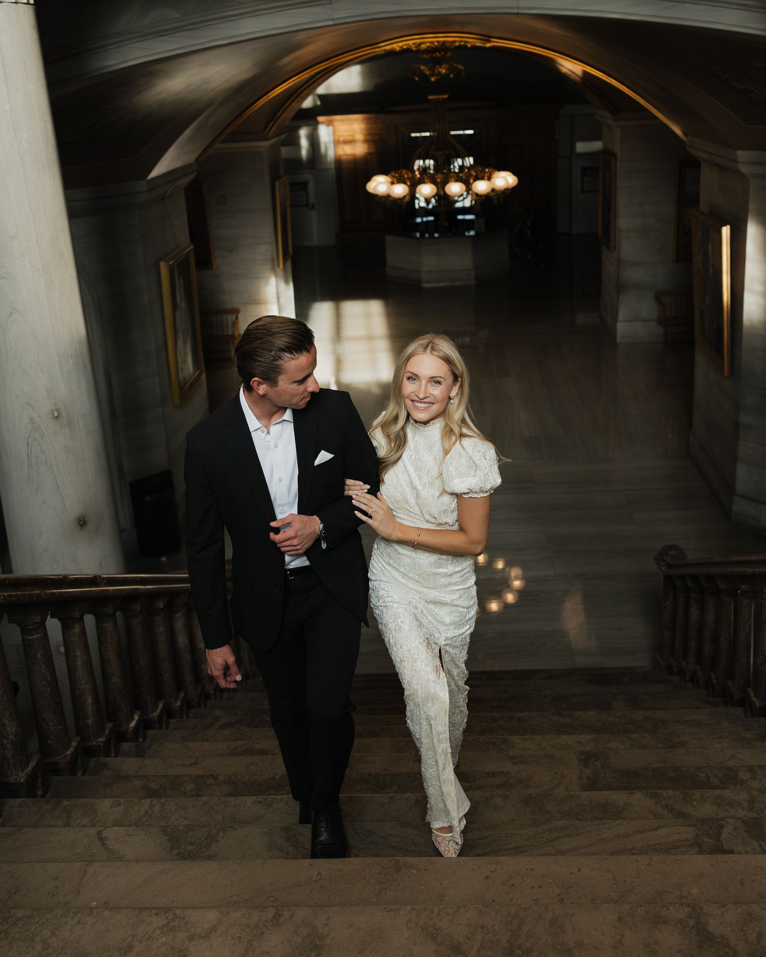 A couple walks together in a dimly lit rustic venue hallway during their engagement celebration.