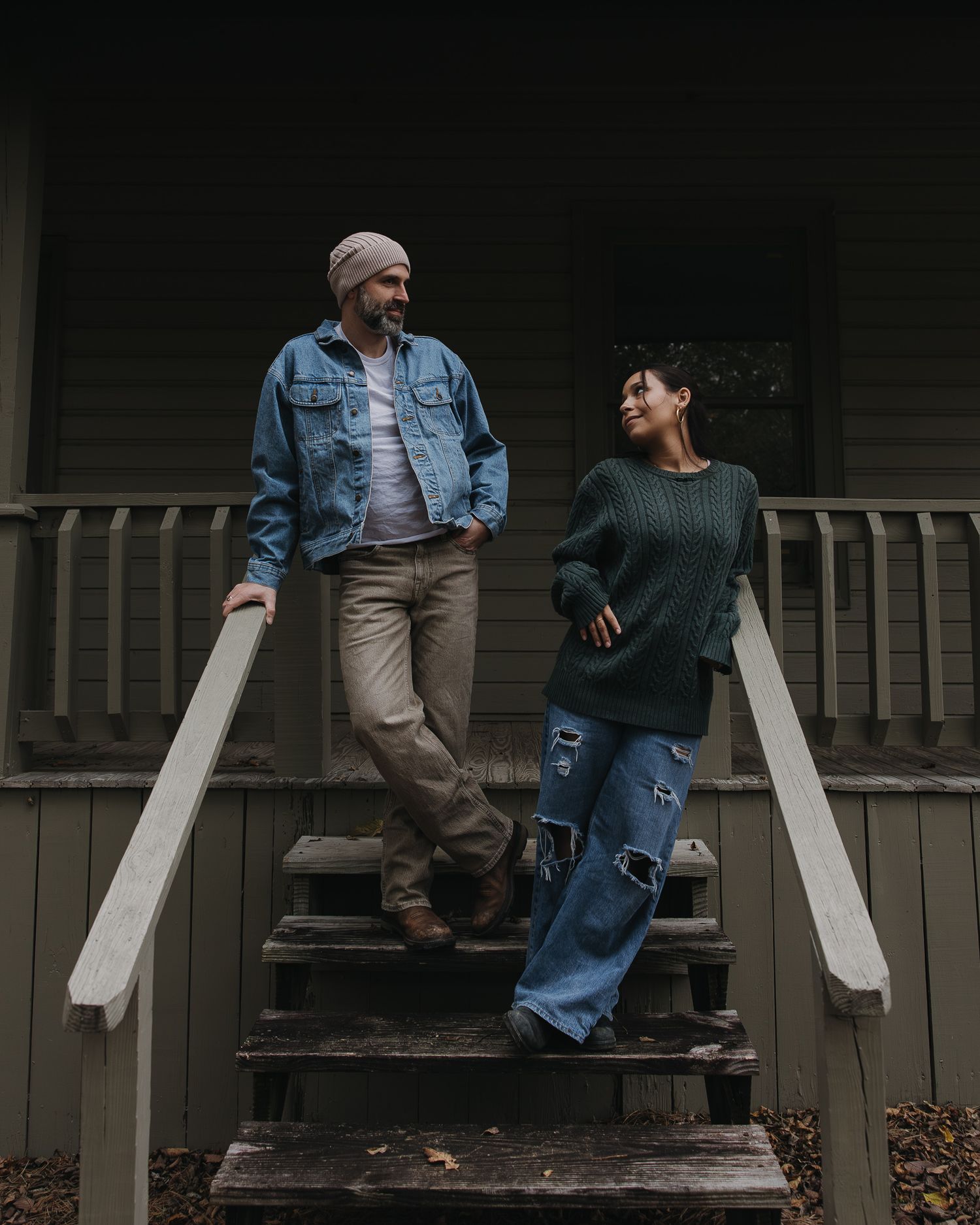 Two people sitting casually on wooden porch steps in casual autumn attire.
