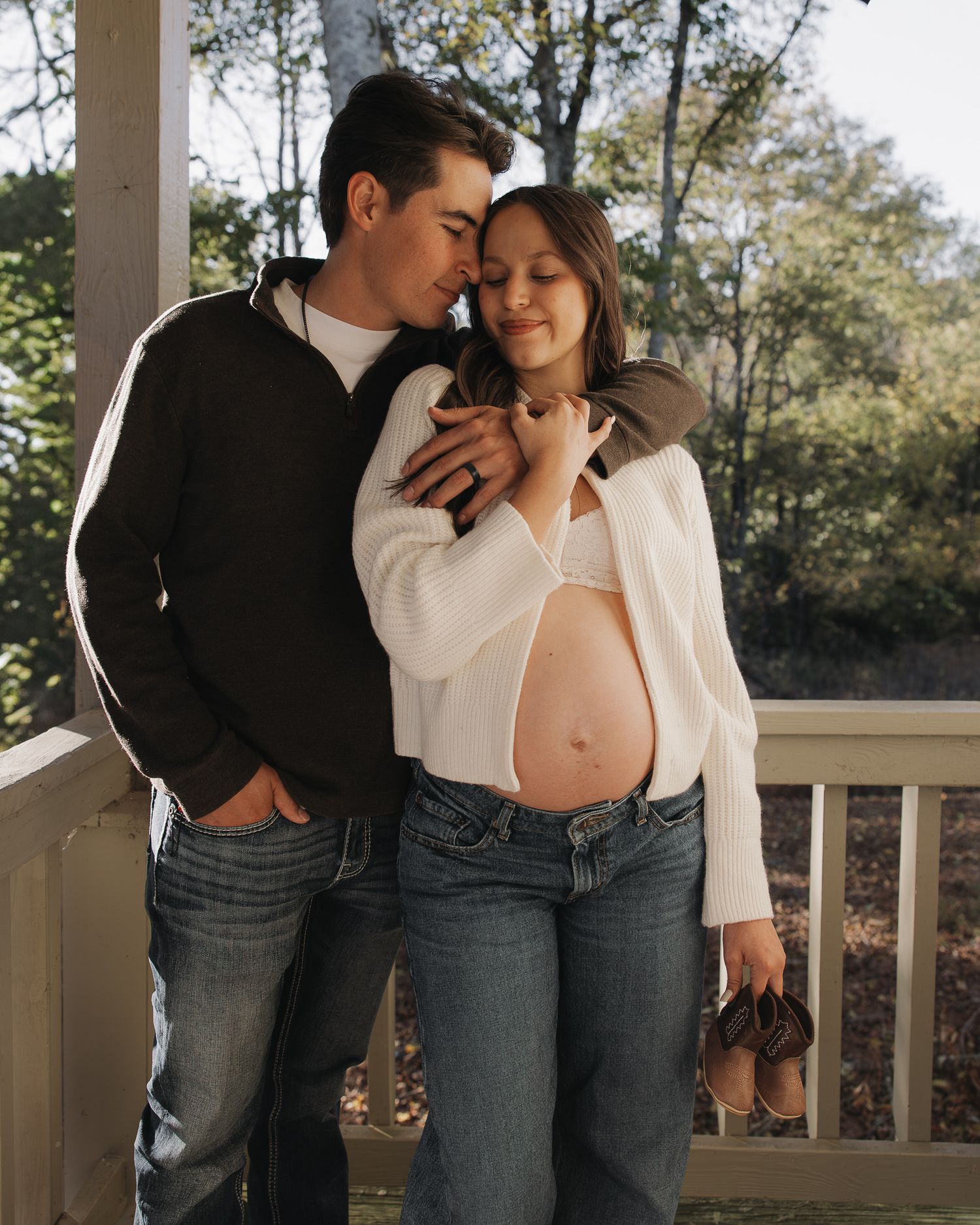 Sunlit maternity photos on a porch featuring tender moments between expecting parents.