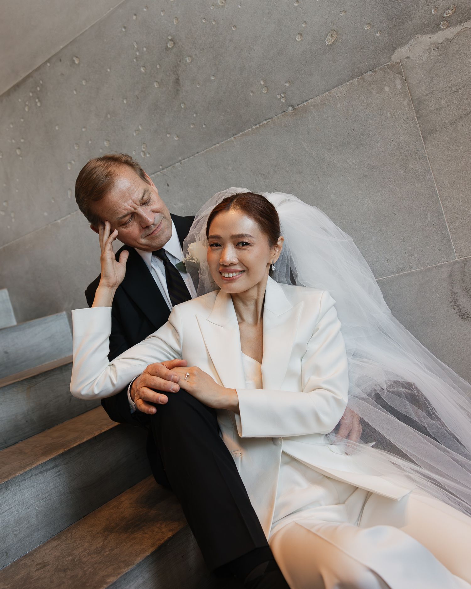 Bride in white blazer and veil sits on steps with groom in black suit during wedding photo session in the Nashville Tennessee State Capitol.