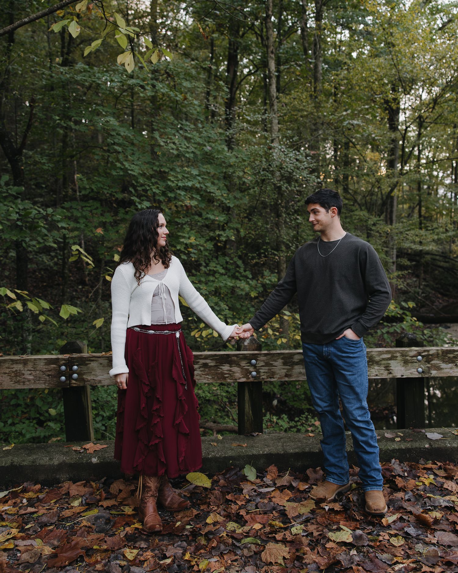 Couple interacting playfully on a leaf-strewn path surrounded by autumn trees.