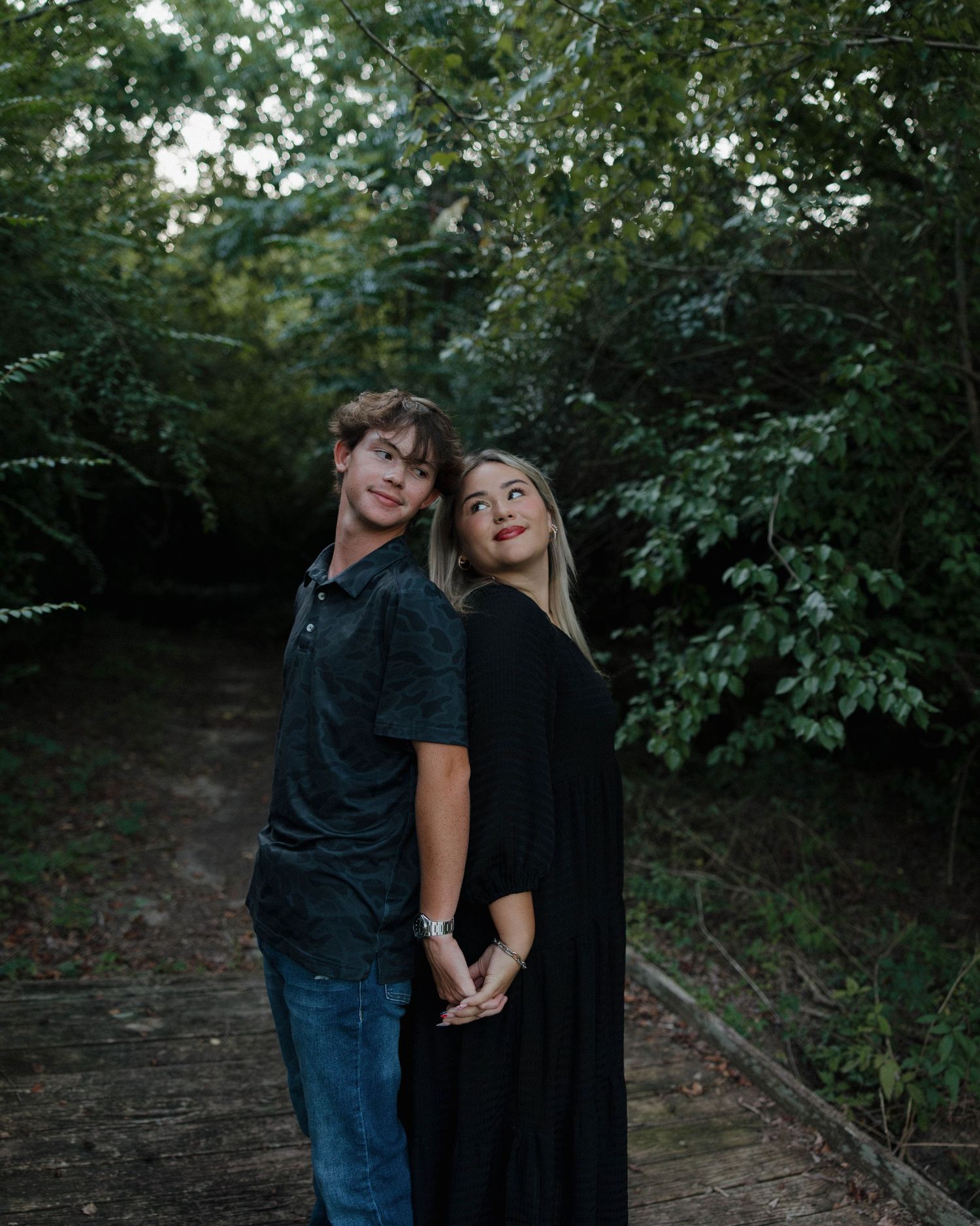 Couple sharing playful moments together in a wooded area during an outdoor photoshoot.