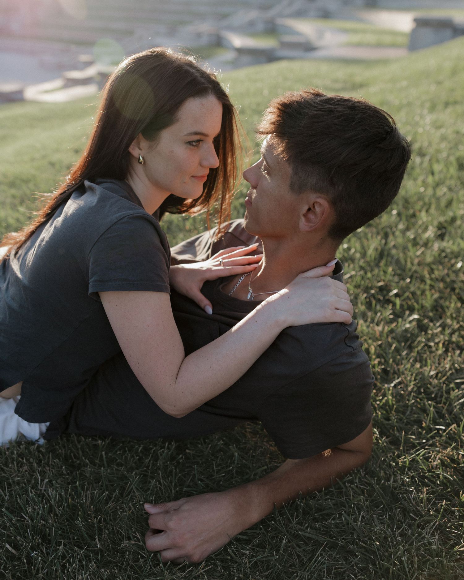 Tender moment between couple cuddling on grass in afternoon light.