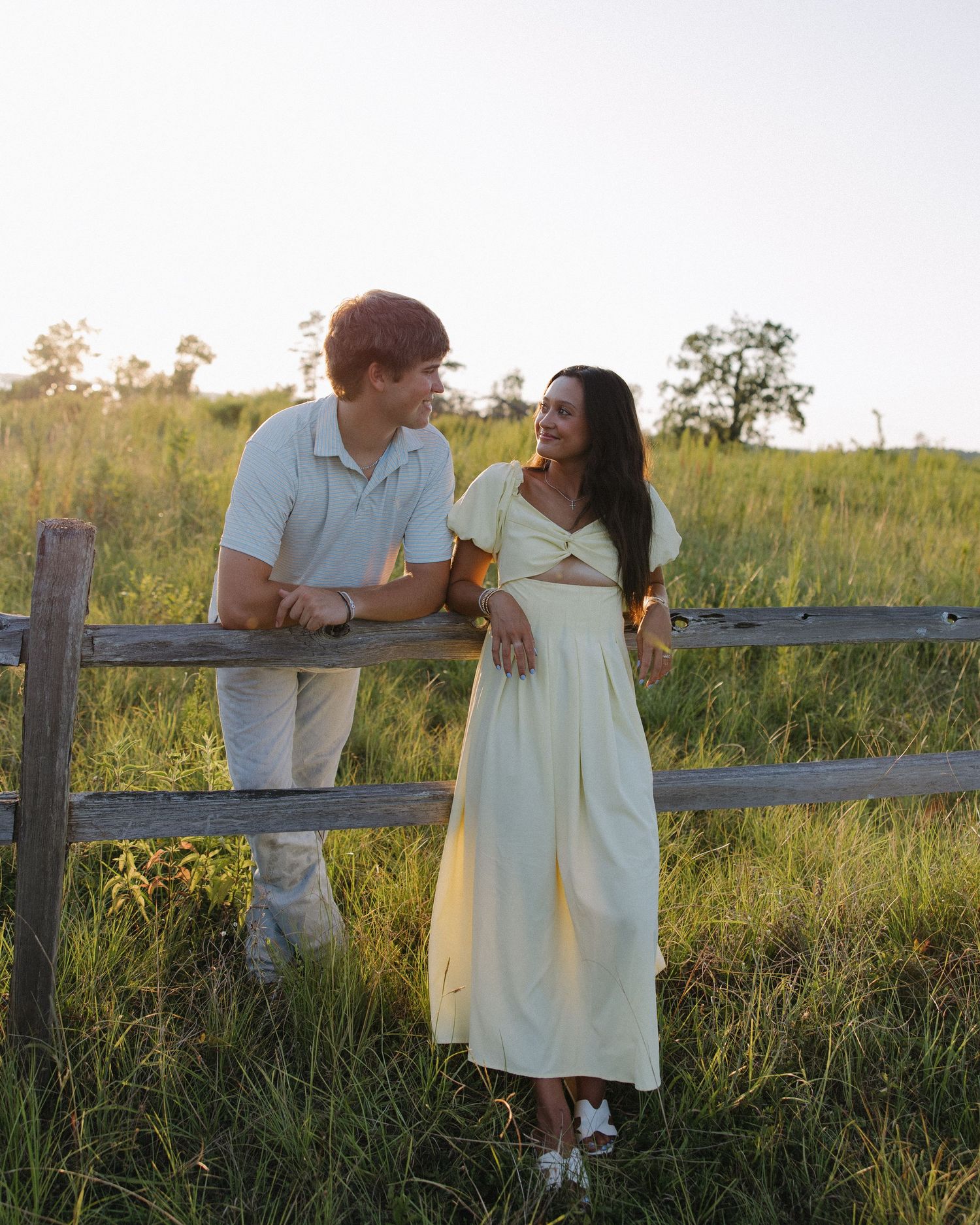 A couple sharing a tender moment while leaning against a wooden fence in a rural setting.