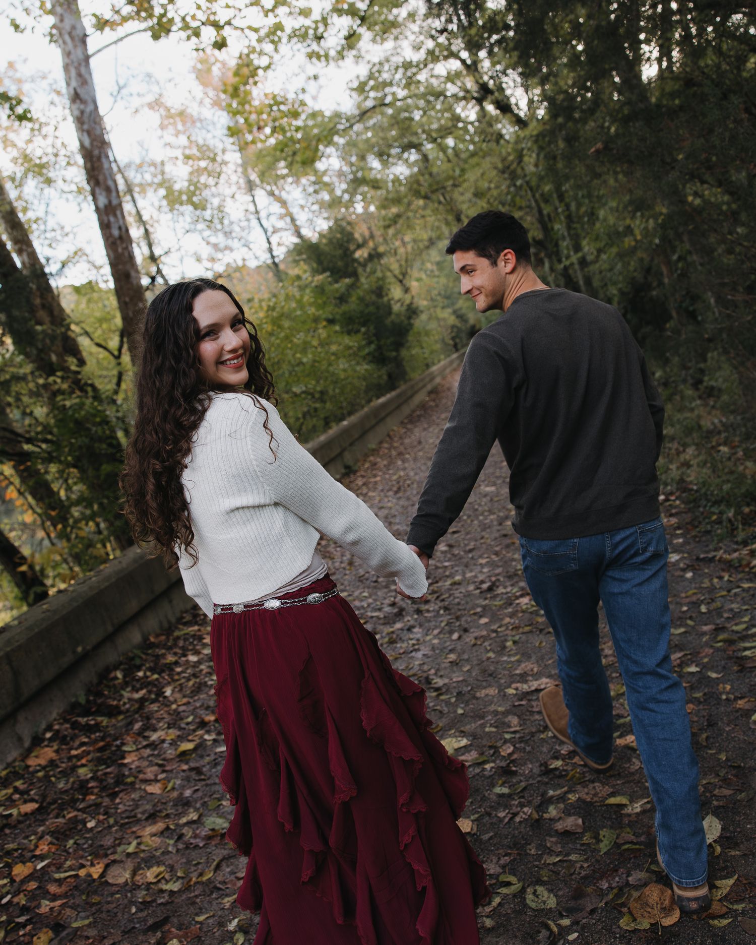 Couple walking and laughing together on leaf-covered autumn trail.