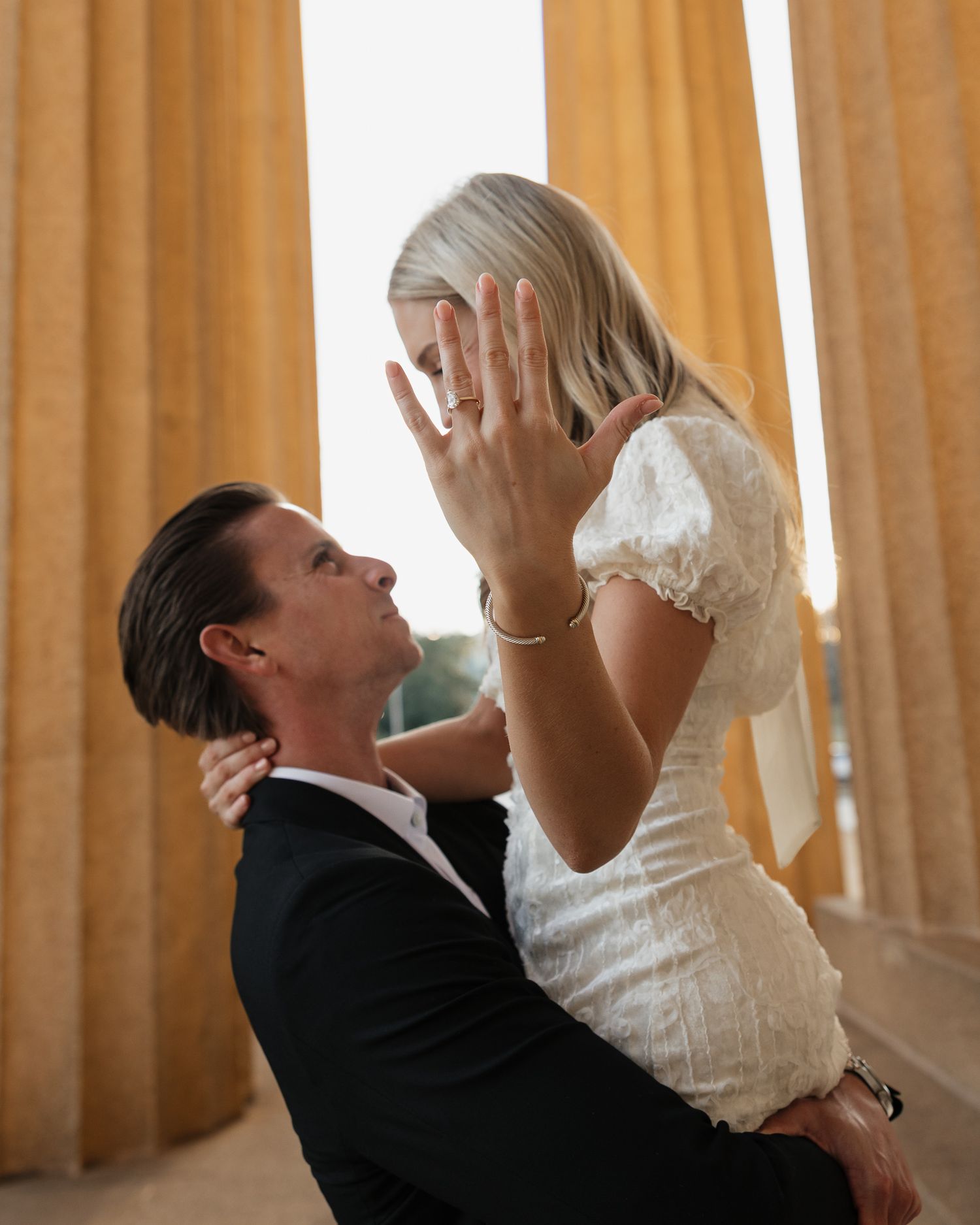 A couple in formal attire dancing together in a romantic sequence while the woman shows her engagement ring.