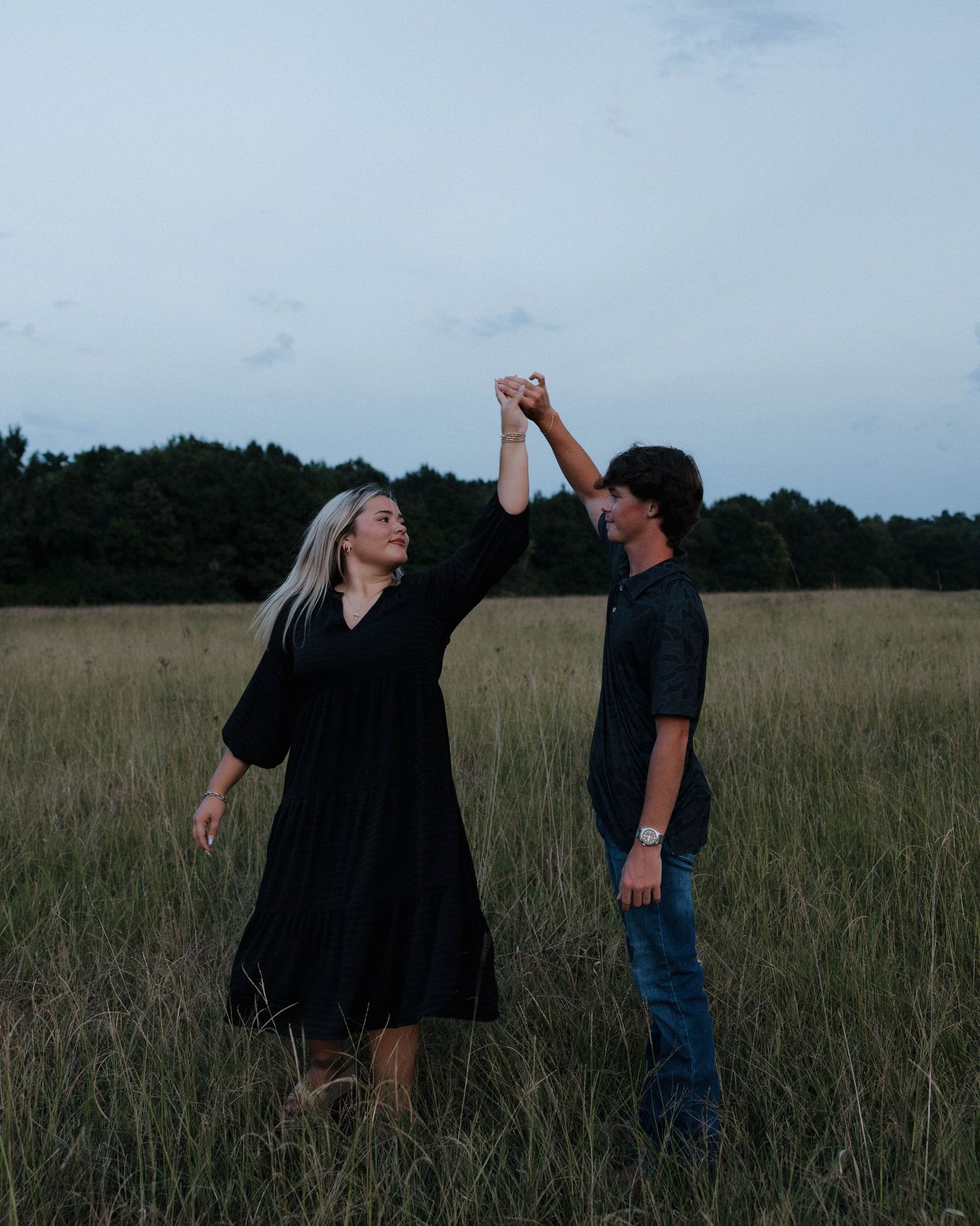 Couple dancing and twirling in a meadow during moody evening light.
