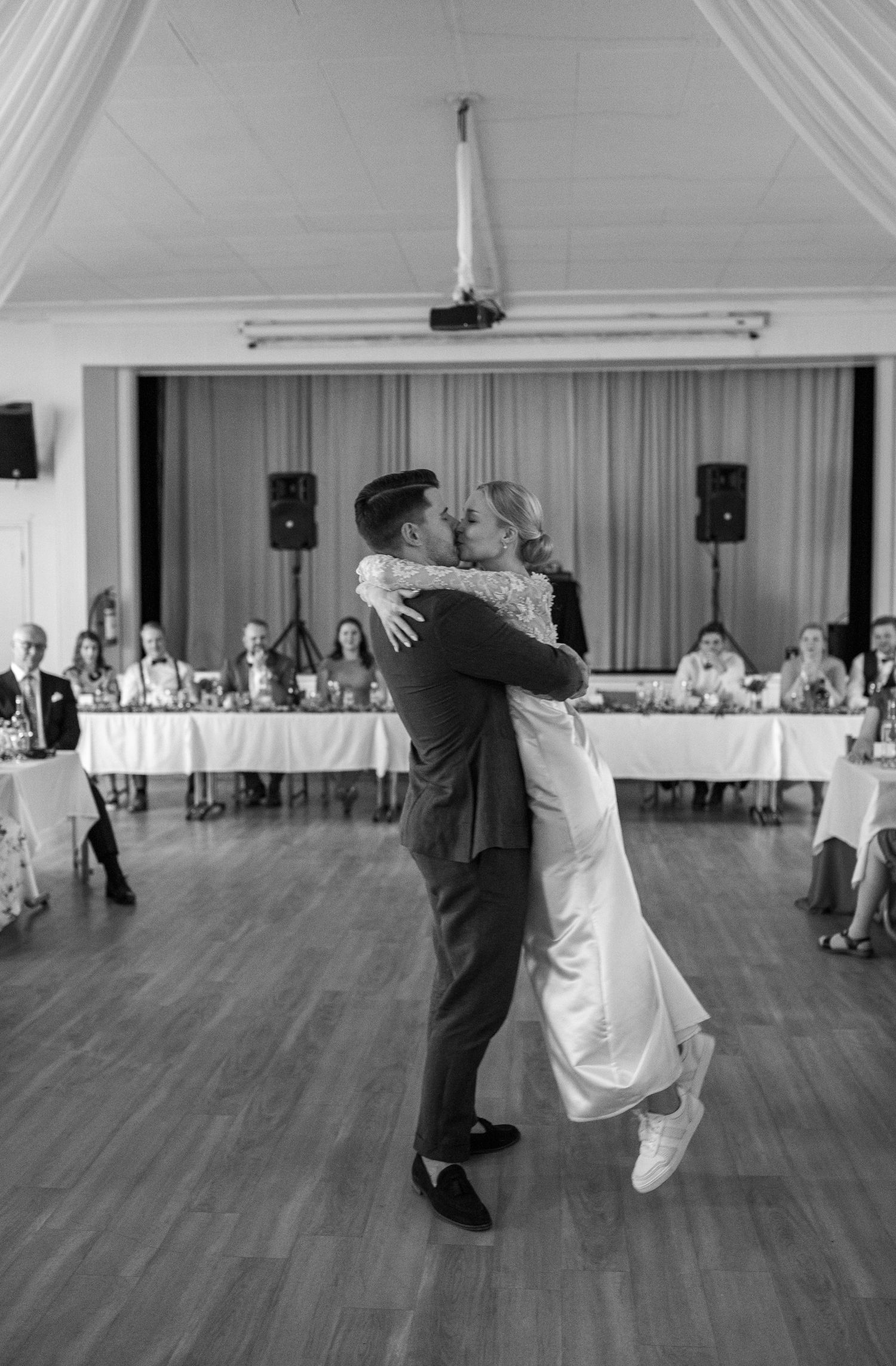 Black and white photo of groom lifting bride during emotional first dance at wedding reception.