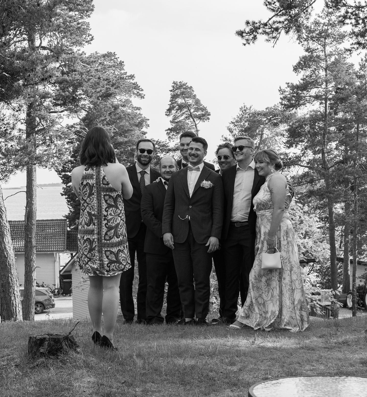Black and white photo of wedding guests posing together outdoors among tall pine trees.