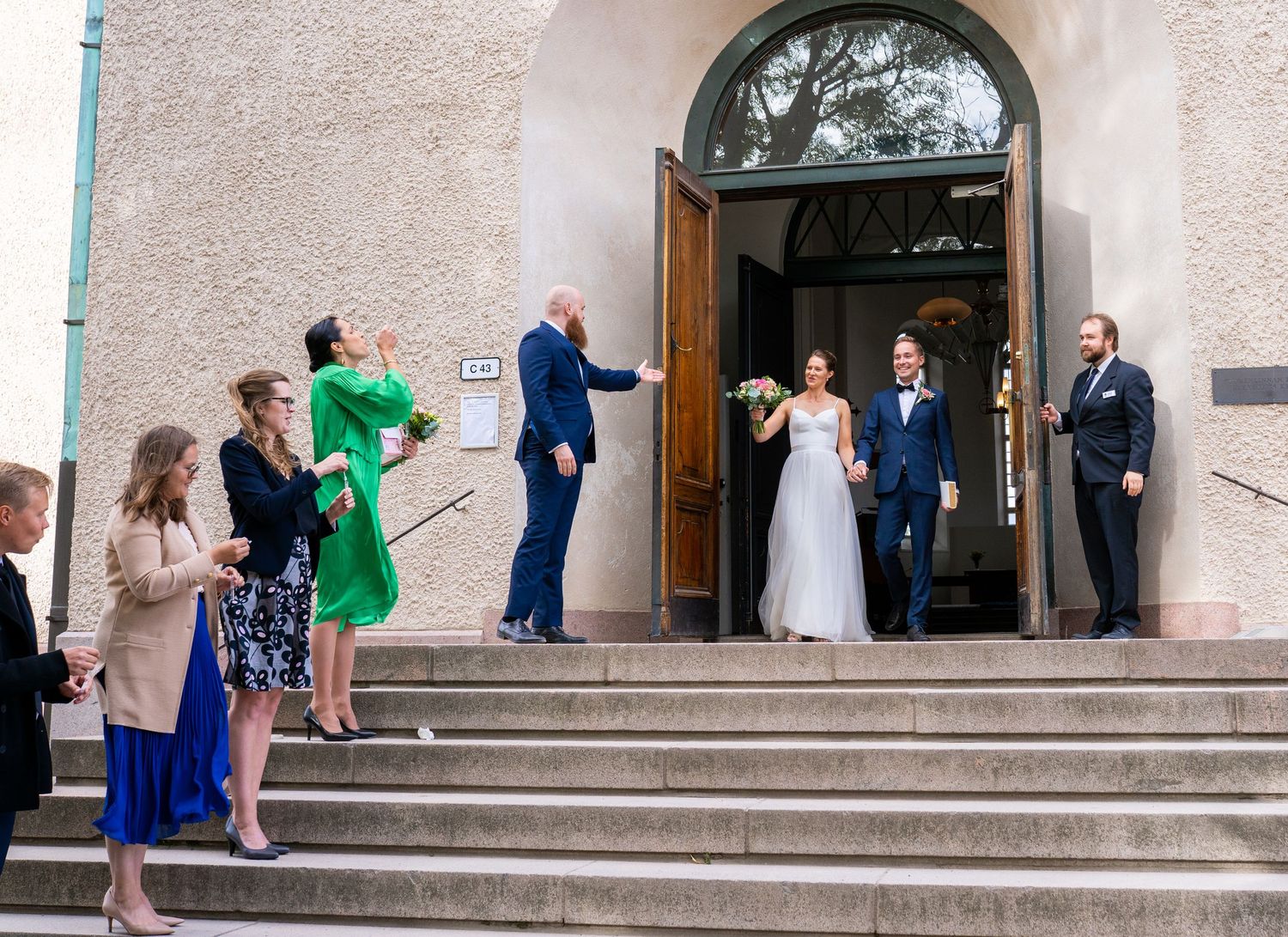 Newlyweds exit church doors greeted by cheering guests on stone steps.