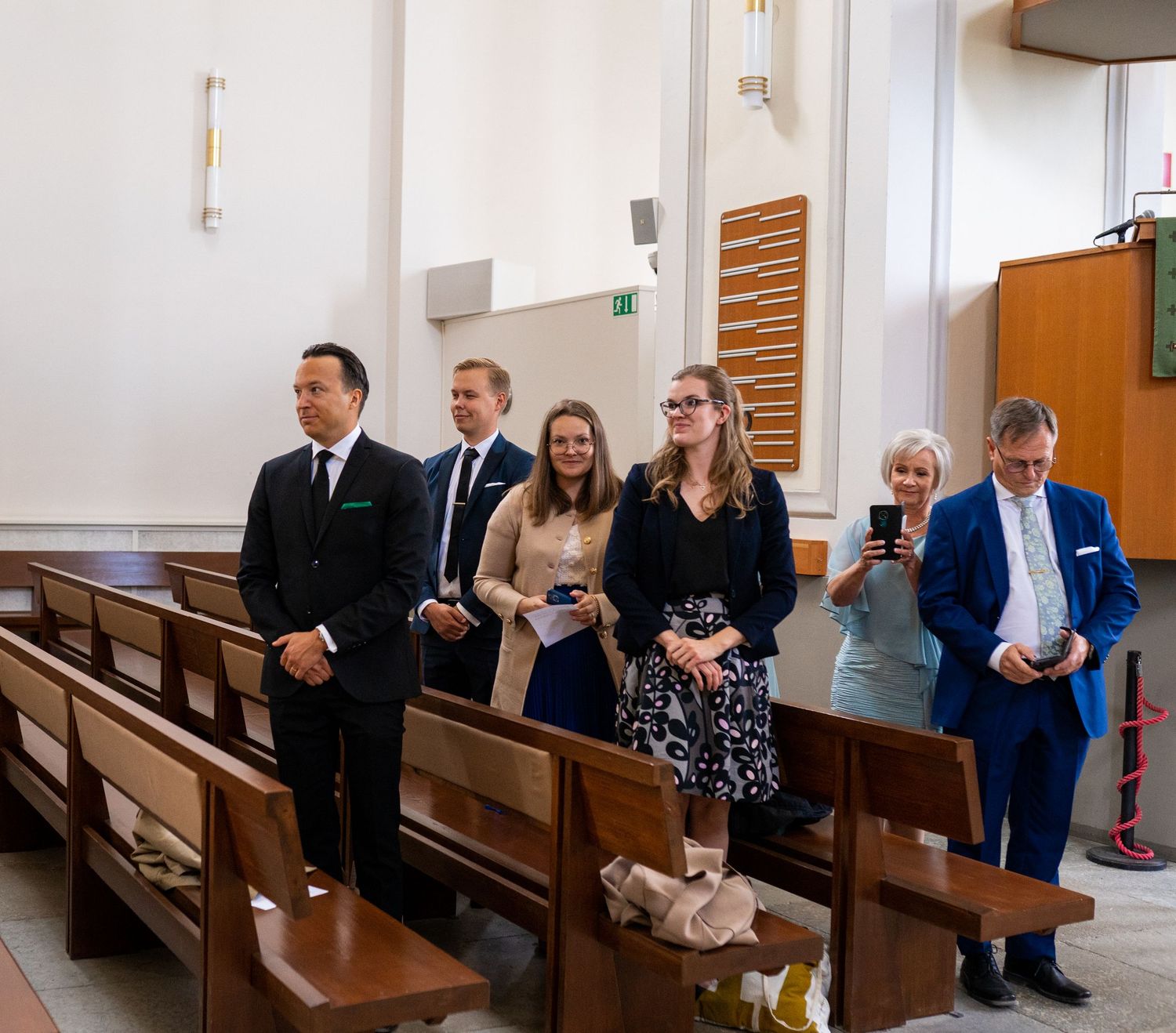 Wedding guests standing in church pews dressed in formal attire during a ceremony.