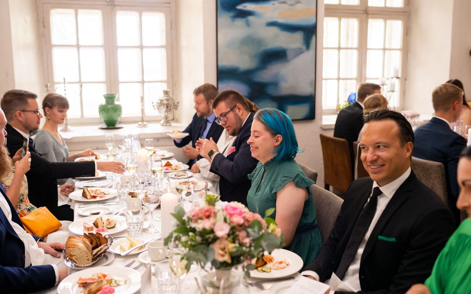 Wedding guests with colorful hair laughing and dining at a long decorated reception table.