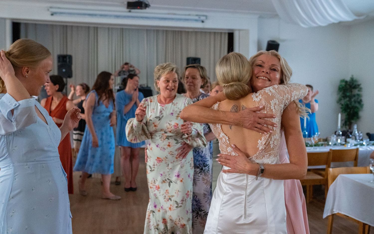 Wedding guests share warm hugs and celebrate on the dance floor at an elegant indoor reception venue.