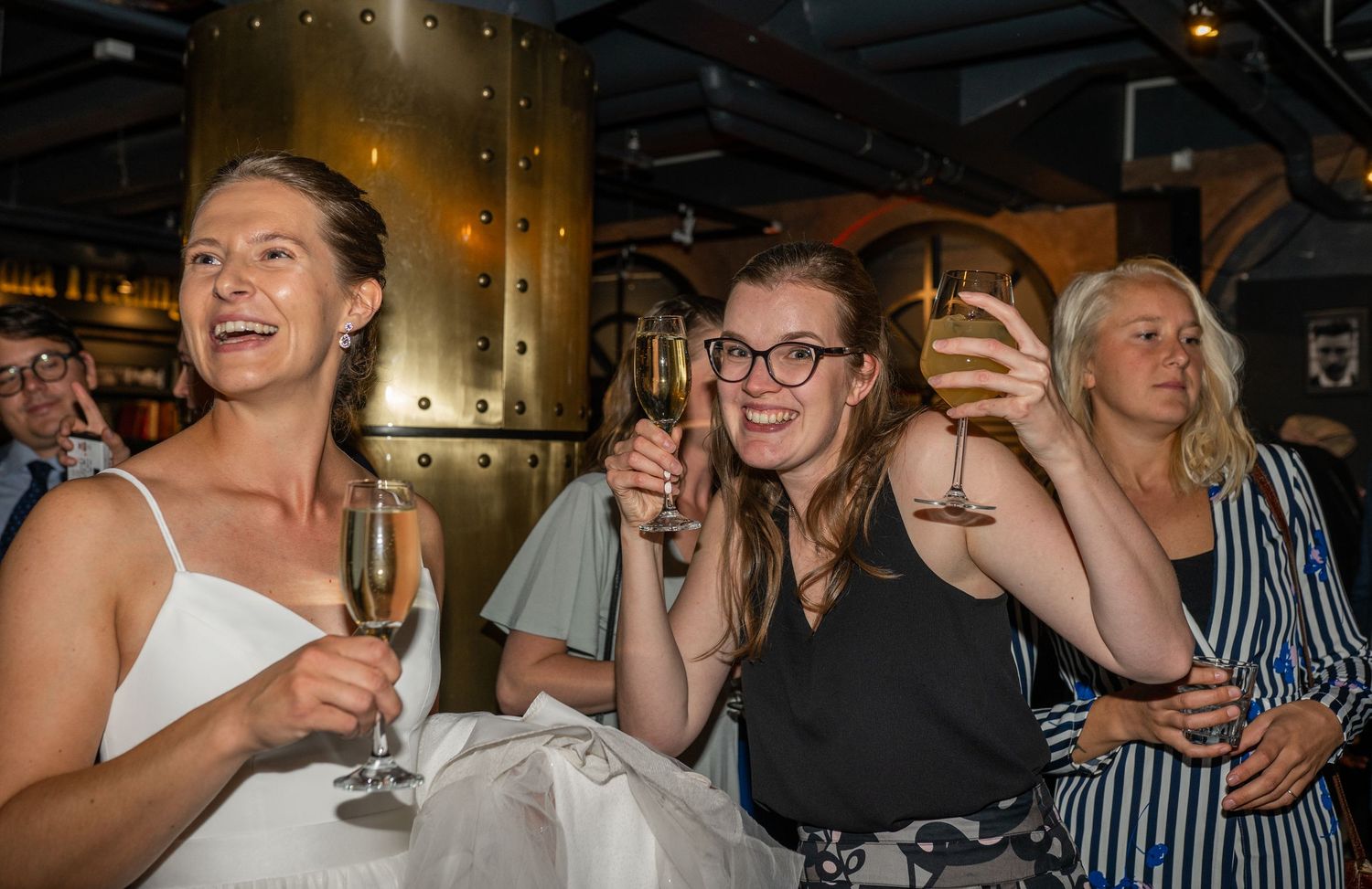 Bride and guests laughing and toasting with champagne glasses at wedding celebration.