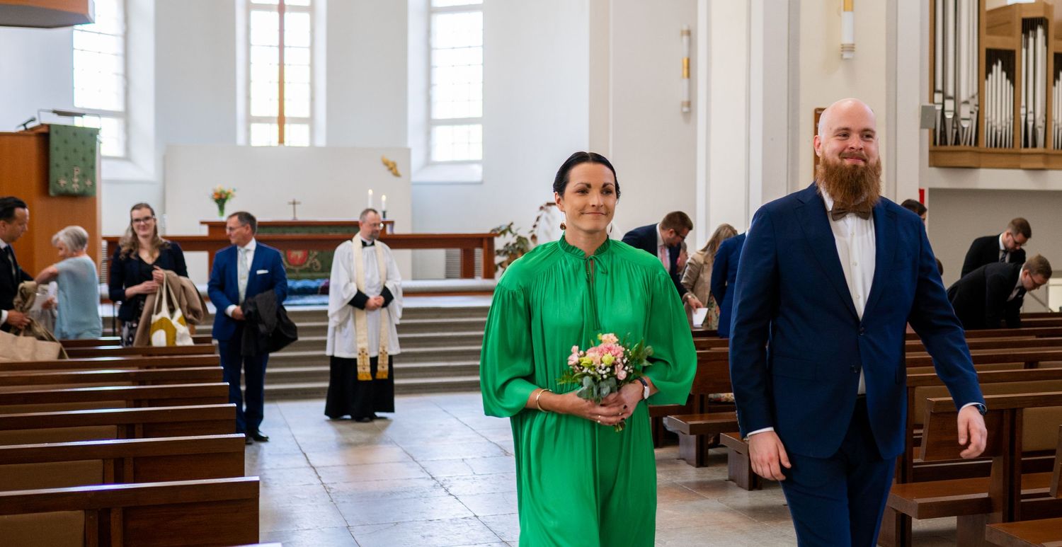 Woman in green dress and bearded man in blue suit walking in church.