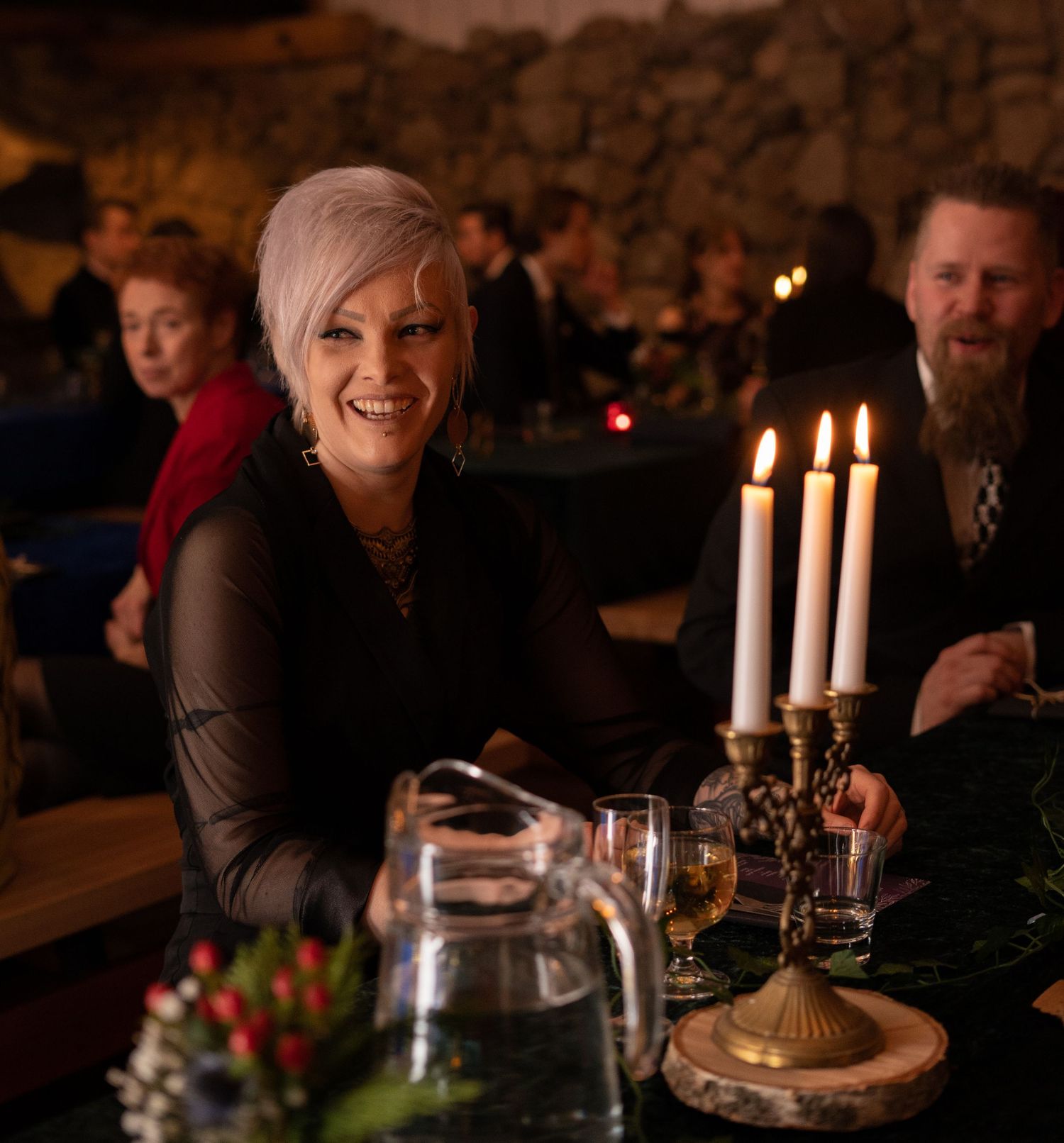 Woman with silver hair smiling at candlelit dinner table in dimly lit restaurant setting.