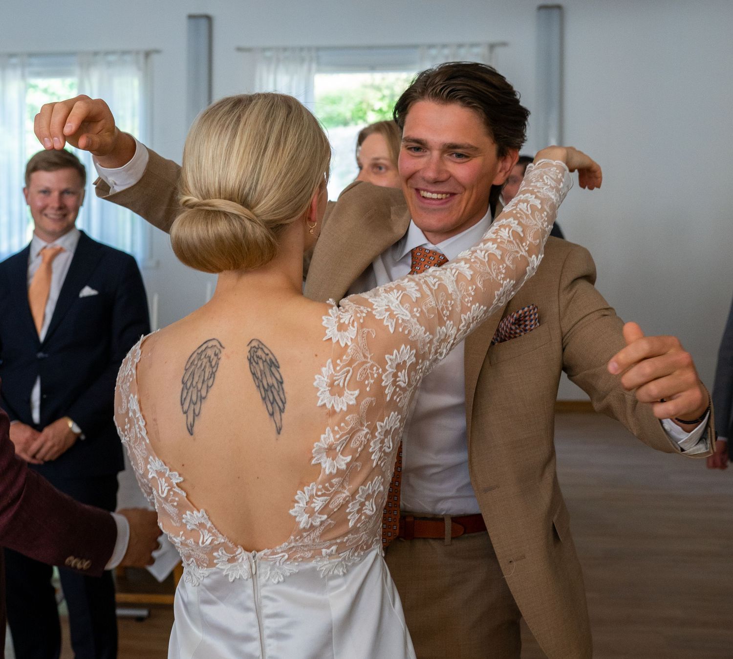 Bride and groom share first dance, bride wearing lace backless gown with wing tattoo.