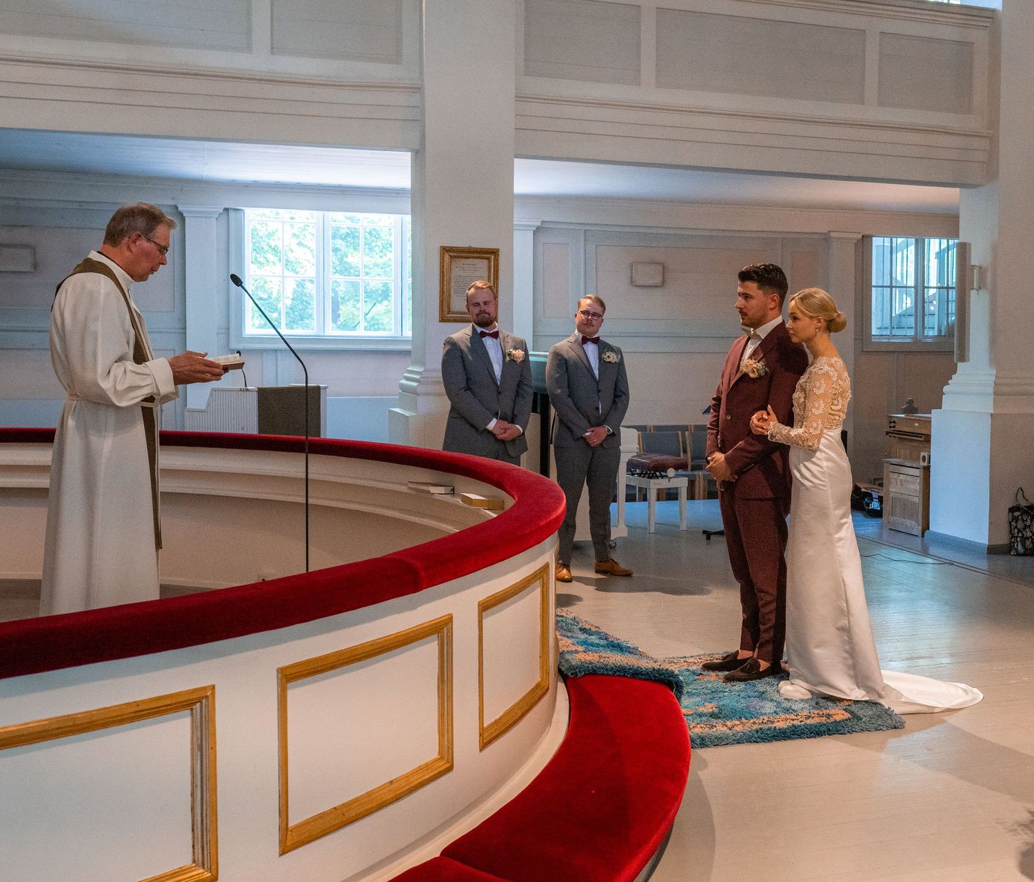 Officiant reads from book as bride and groom stand with witnesses at ornate church altar during ceremony.