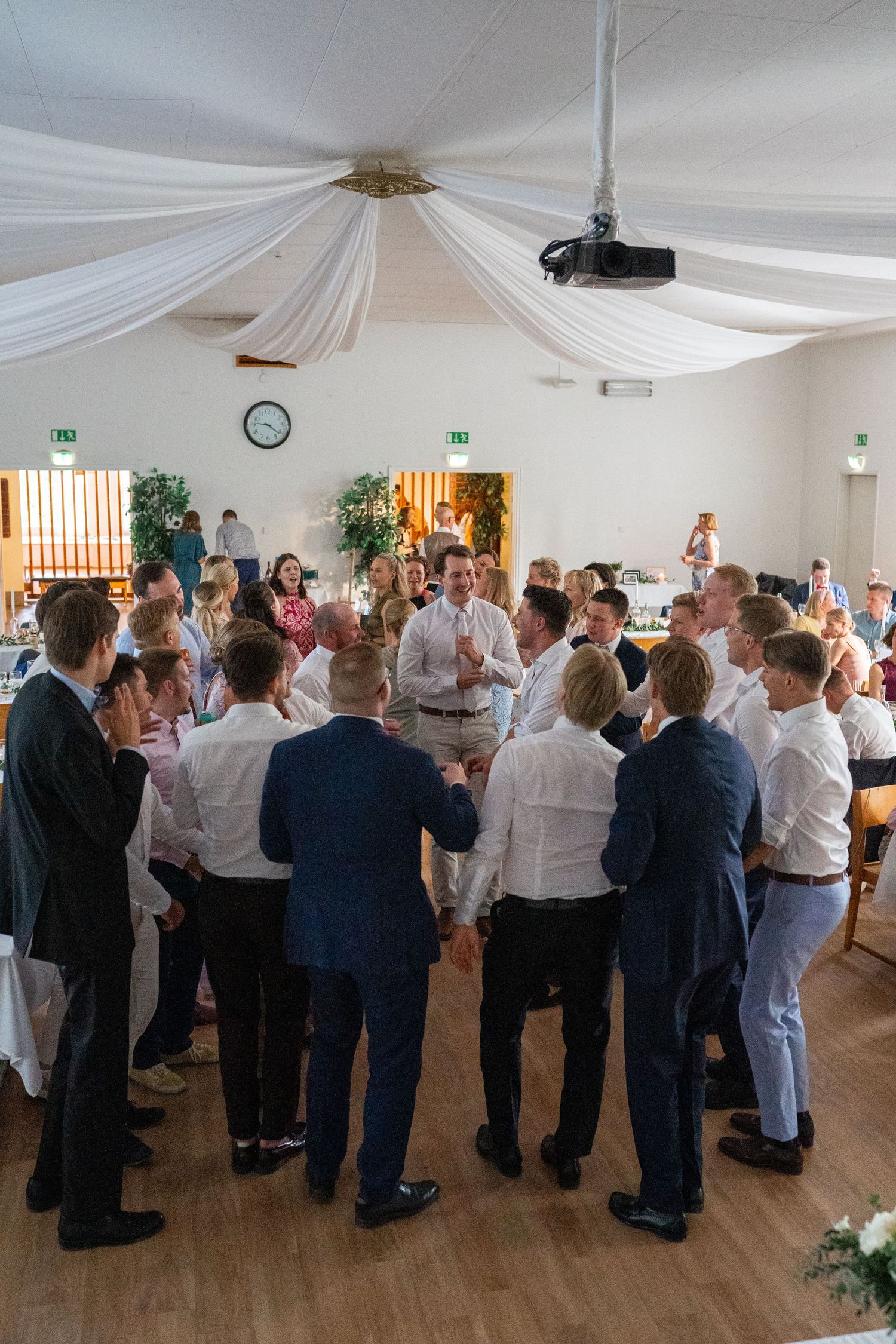Male wedding guests form a large circle on the dance floor during a lively wedding reception celebration.