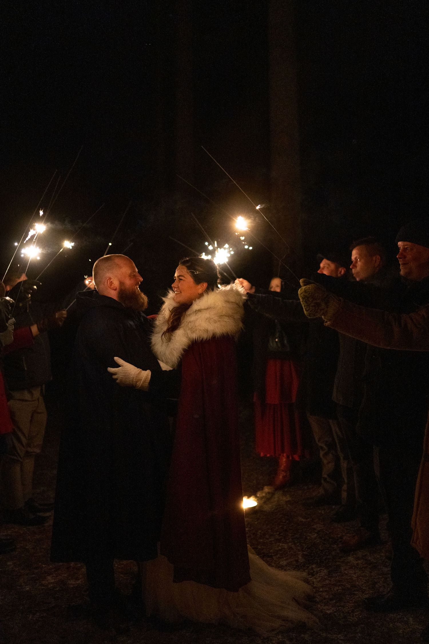 Couple dancing surrounded by sparklers at a winter night wedding celebration outdoors.