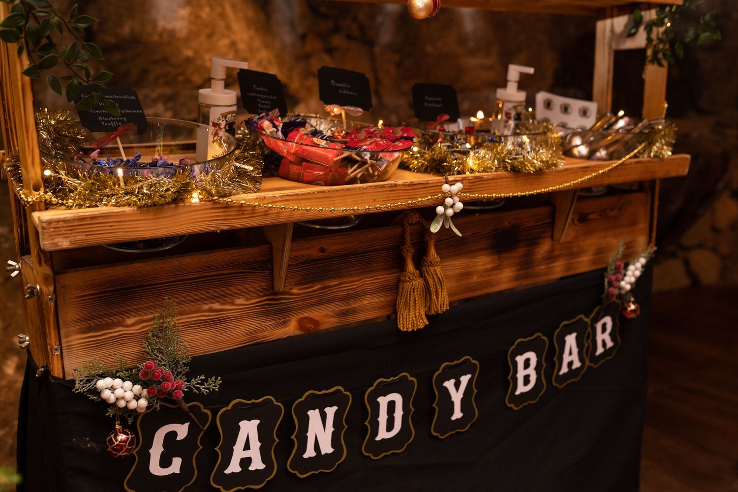 Rustic wooden candy bar display decorated with gold garland and festive treats at a wedding reception.
