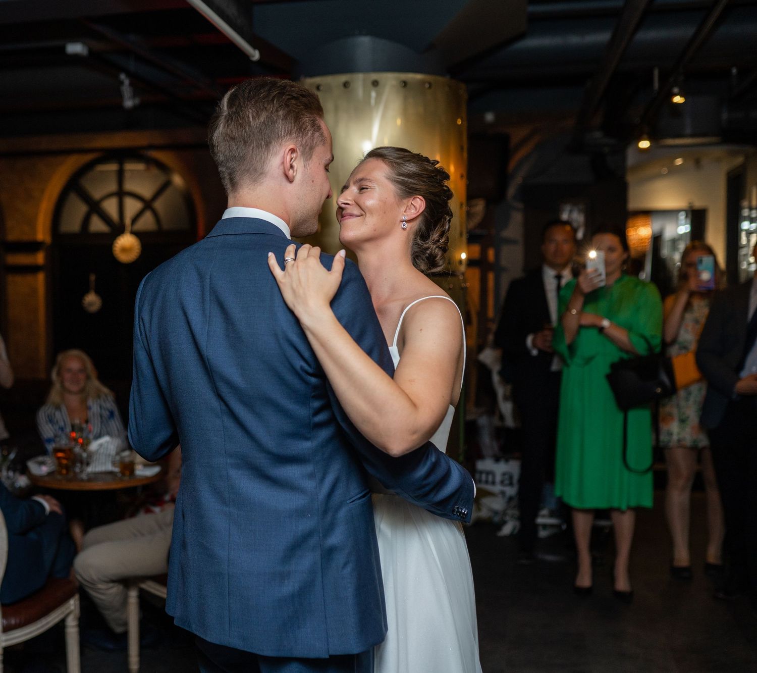 Smiling bride in white gown dancing closely with groom in blue suit during romantic wedding first dance.